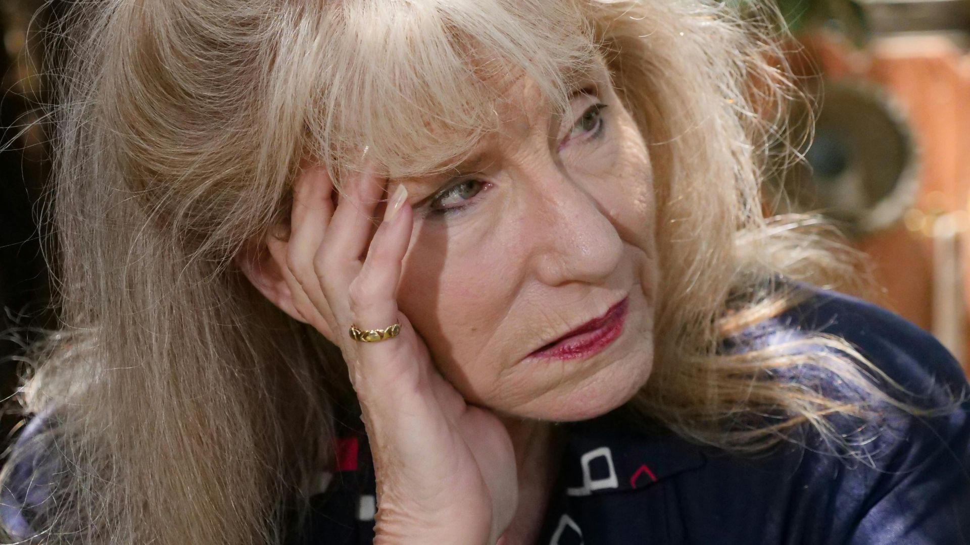 Elderly woman outdoors with a thoughtful expression, hand on face, in natural light.