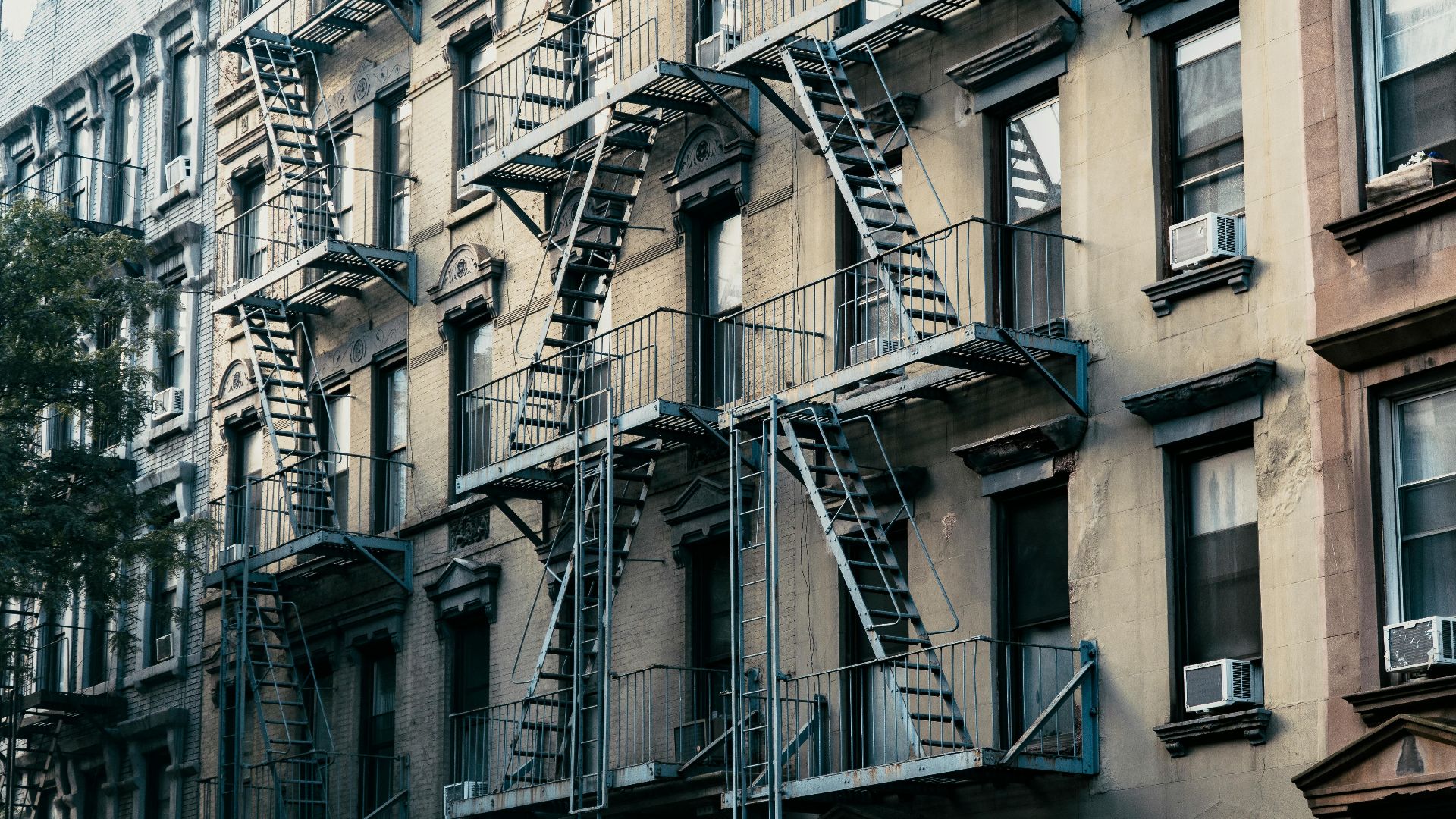 Classic New York City apartment buildings with fire escapes in an urban setting.