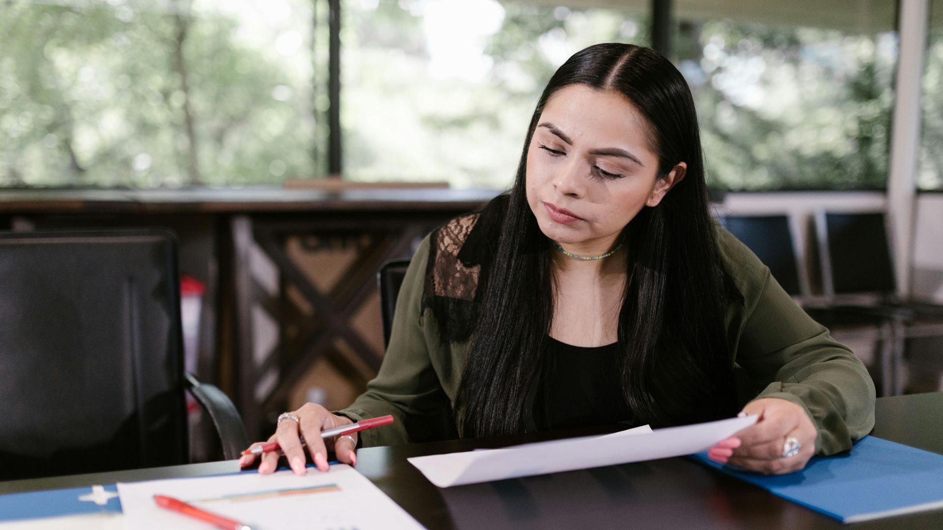 Professional woman in office setting studying documents with concentration.
