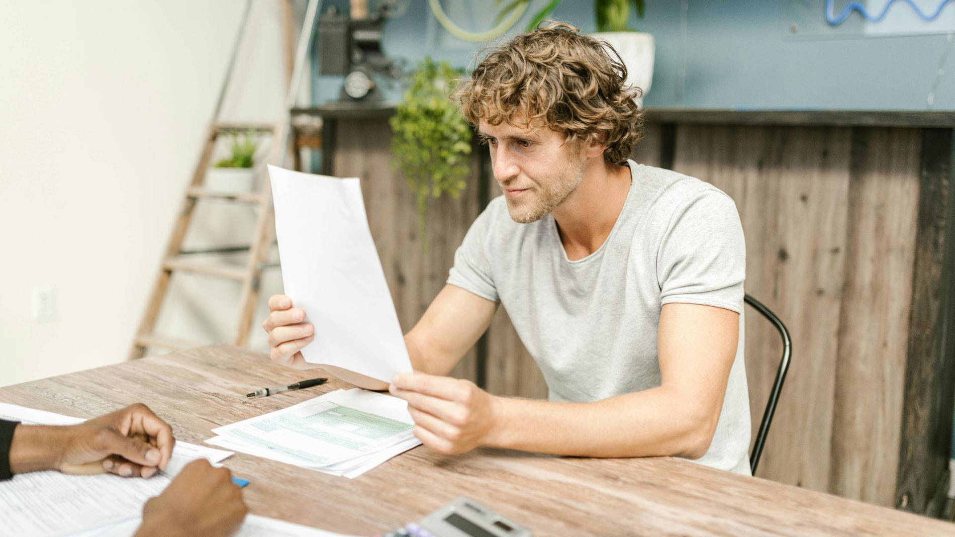 A man with curly hair evaluates documents at a desk, highlighting focused work in a professional setting.
