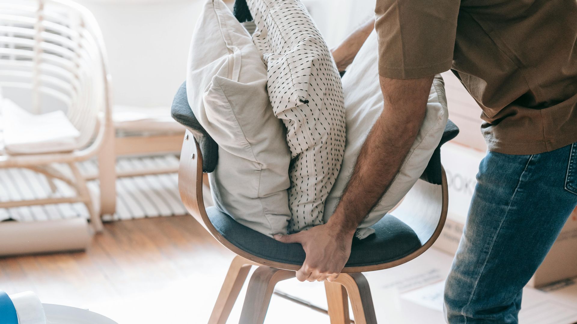 A man packing throw pillows on a contemporary chair indoors, suggesting moving or organizing.