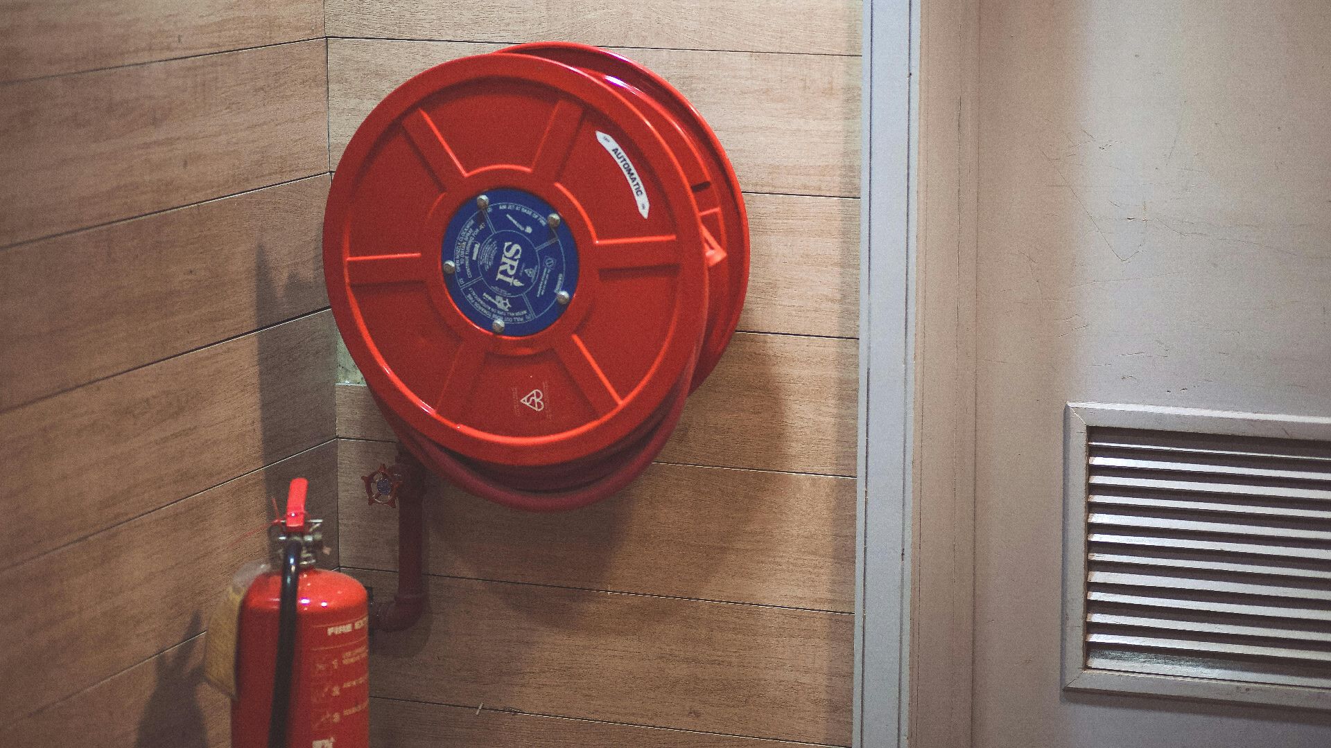 Red fire hose reel and extinguisher inside a building corner.