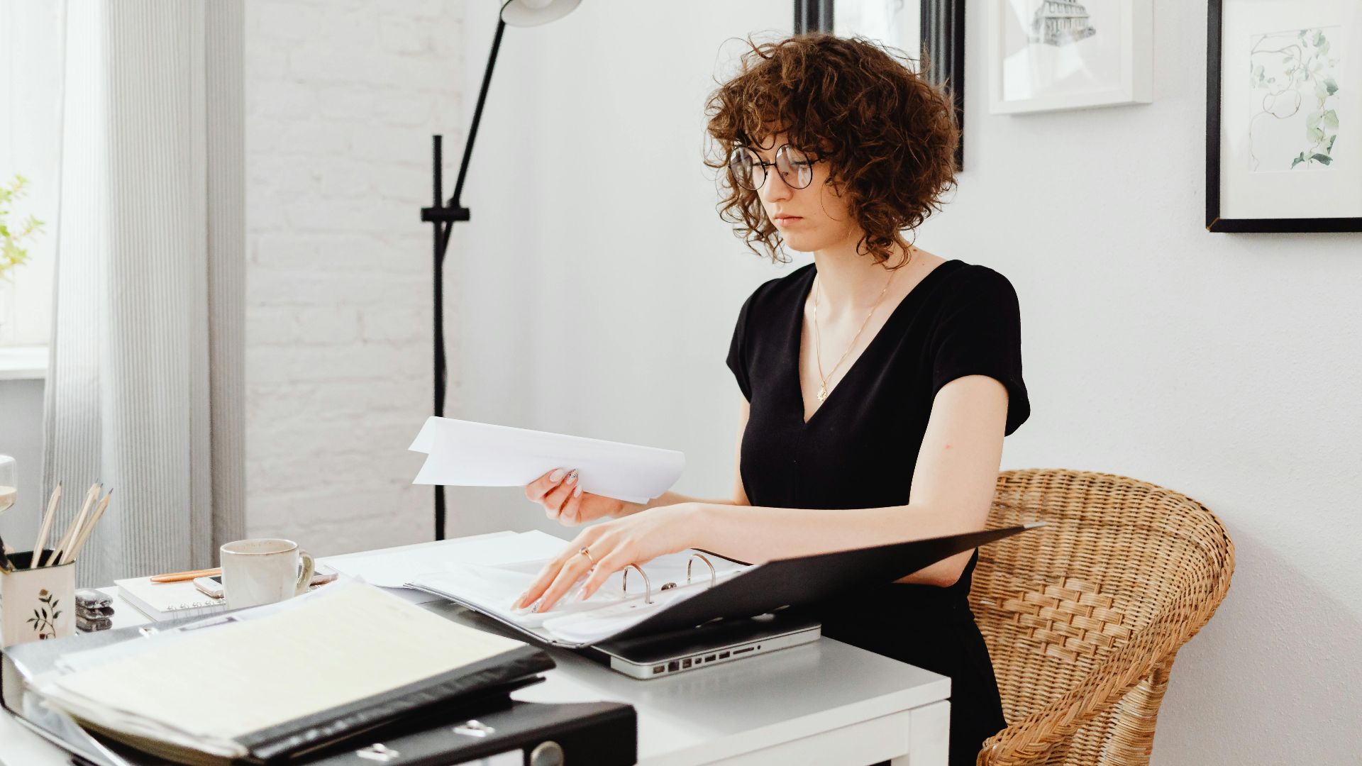 Caucasian woman with curly hair working at home office desk, organizing documents.
