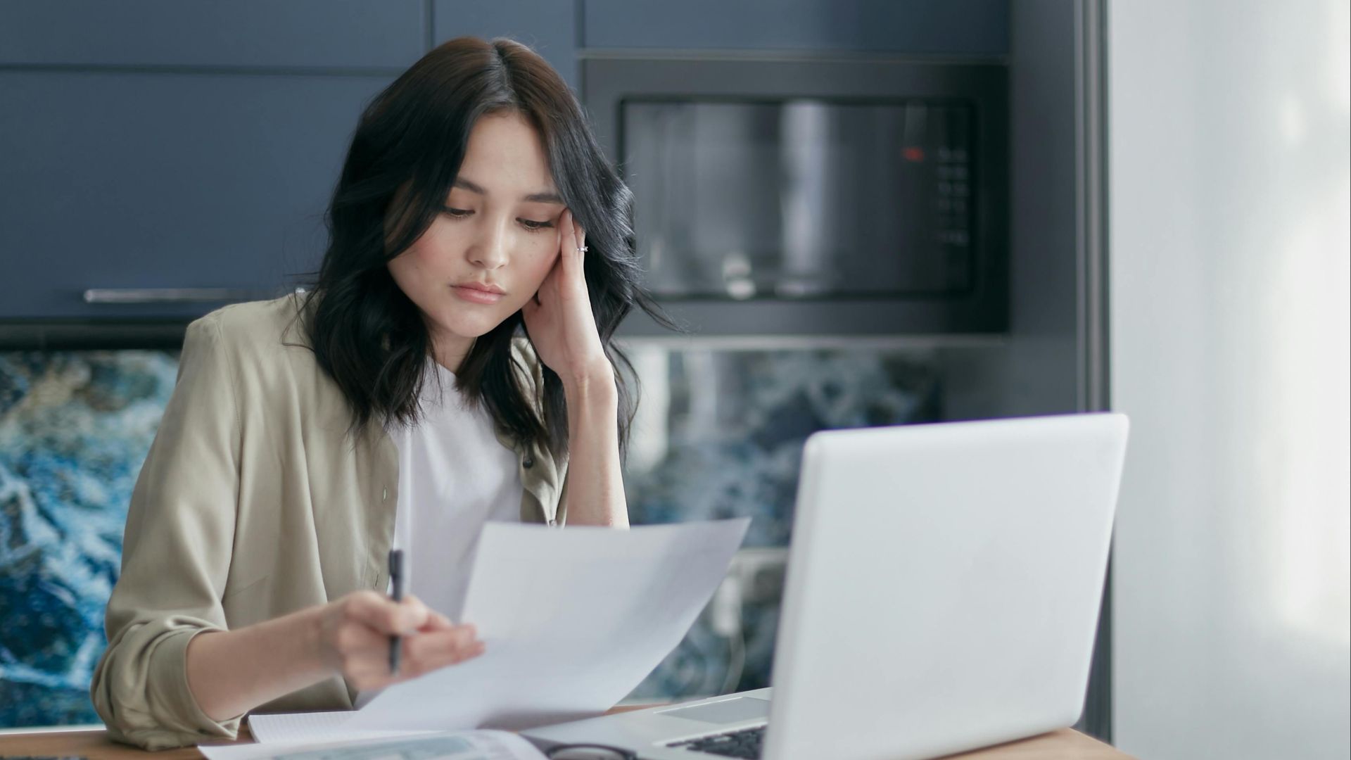 Focused young woman reviewing financial documents with a laptop in a home office setting.
