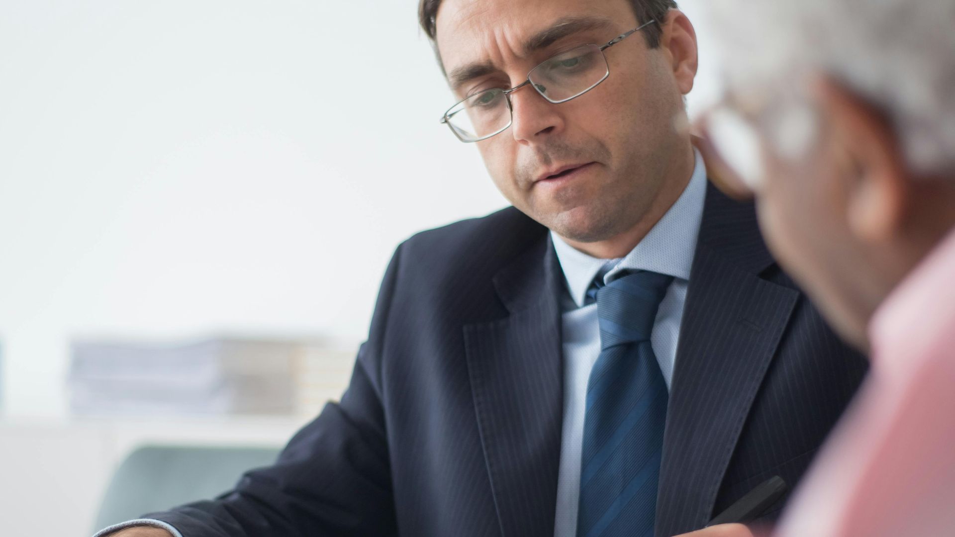 Senior man in discussion with consultant in office setting, reviewing documents.