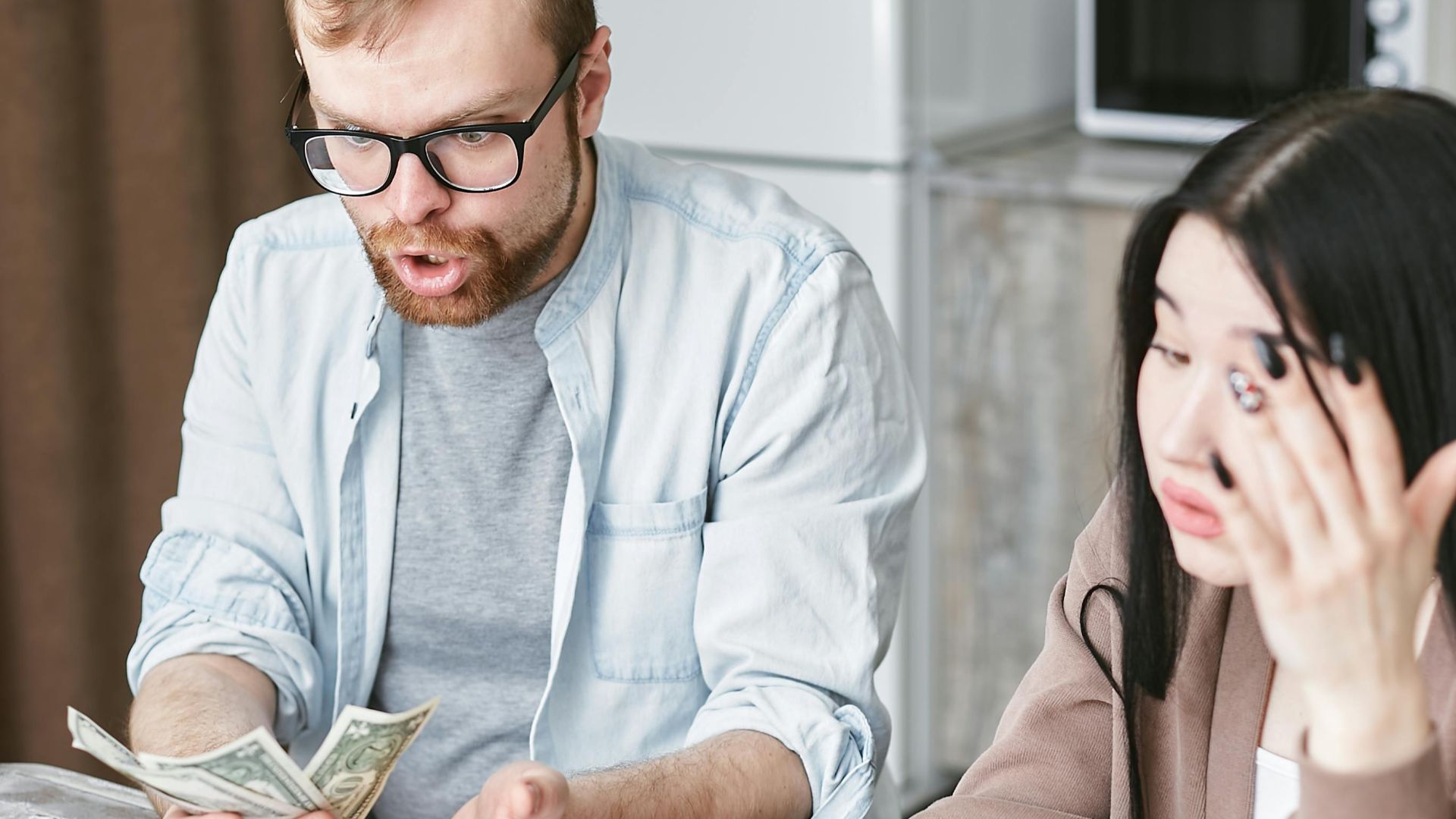 A couple is overwhelmed while handling their finances at home, counting money with stress.