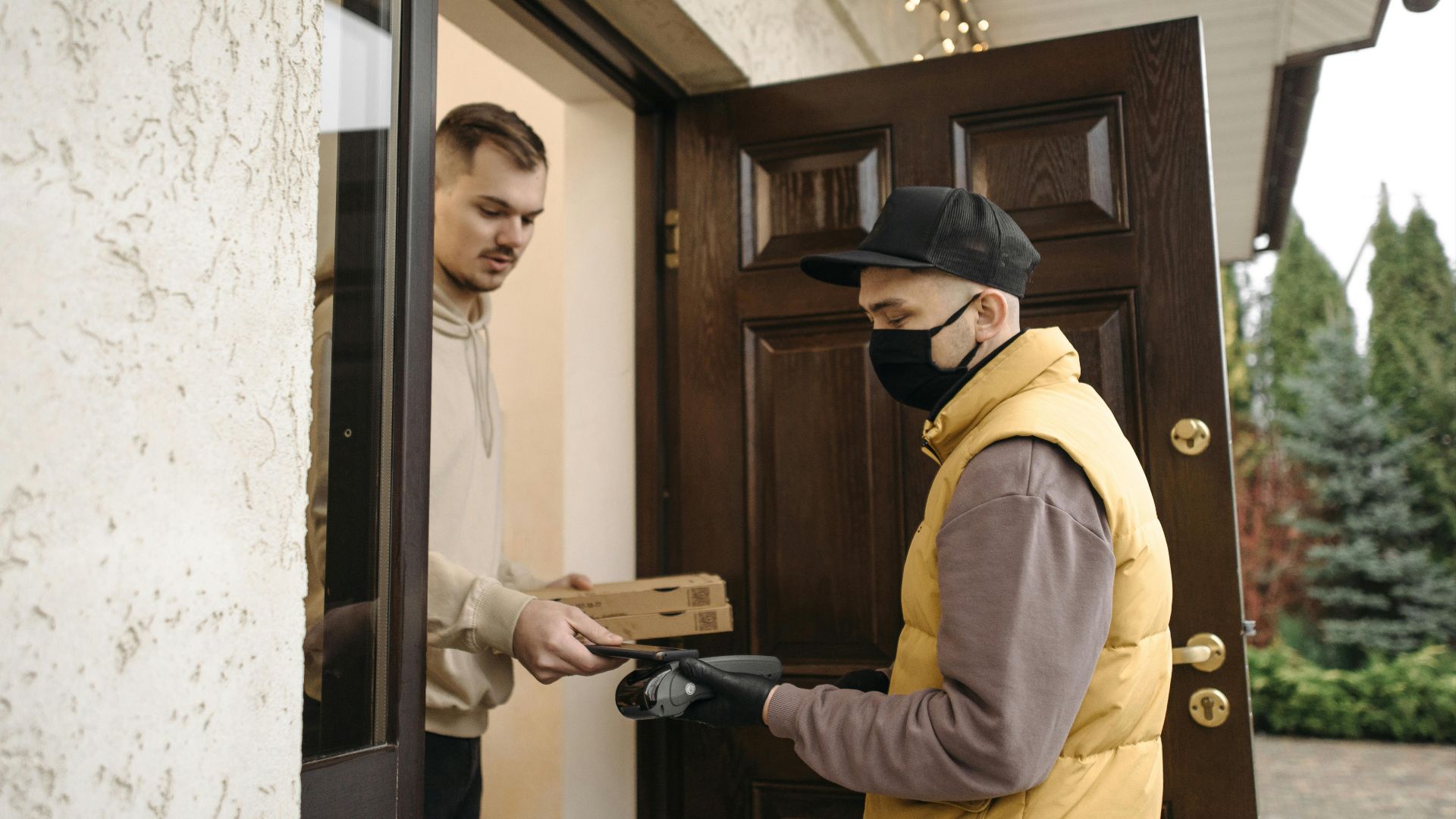 Courier wearing a mask hands a package to a man at home. Safe delivery service.