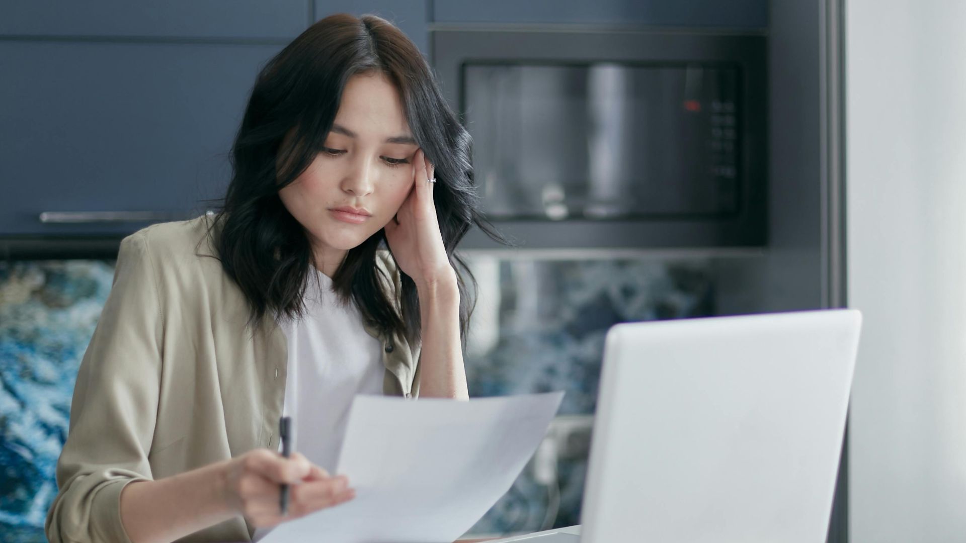Focused young woman reviewing financial documents with a laptop in a home office setting.