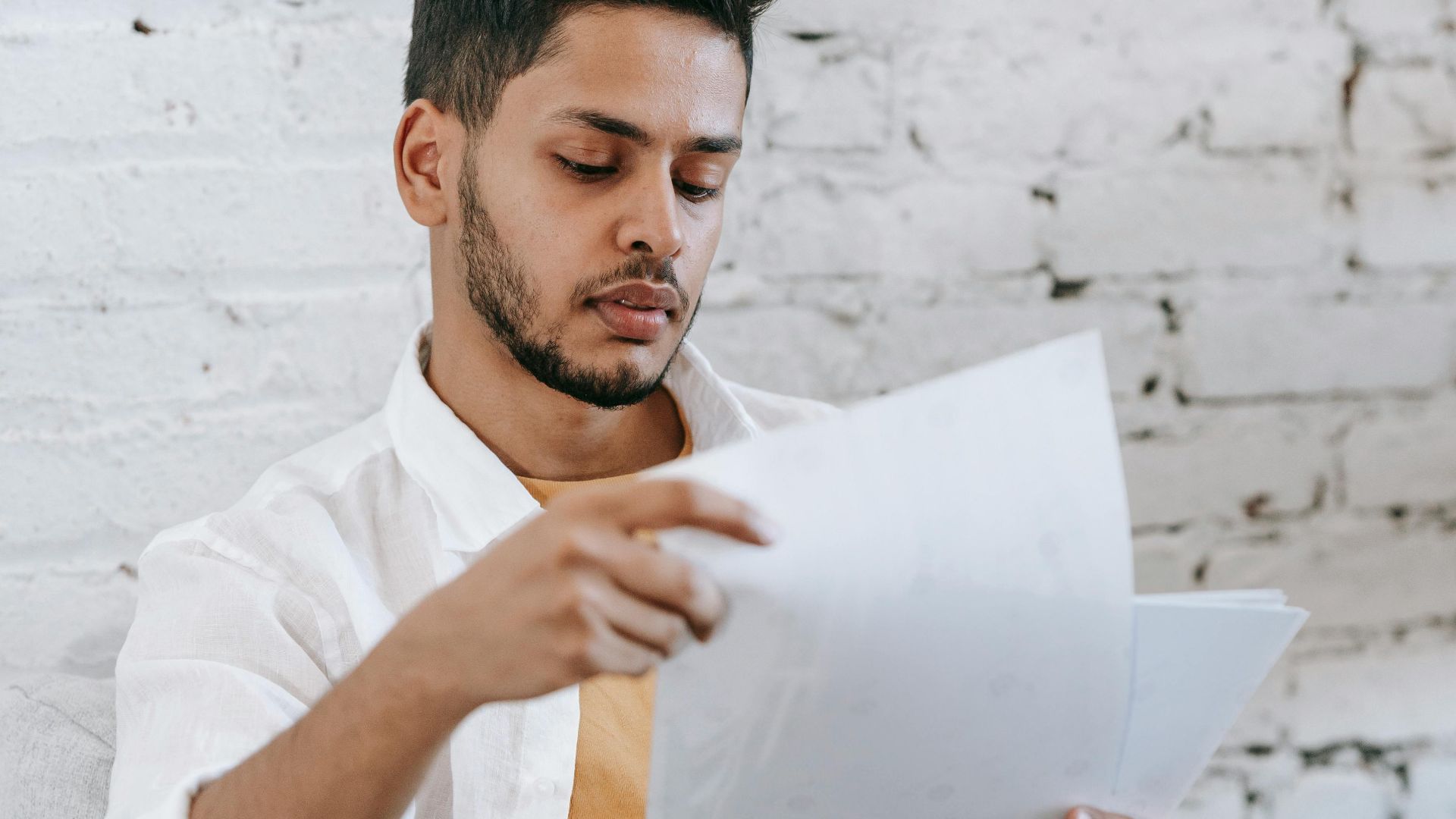 Concentrated young bearded Hispanic male sitting in armchair and analyzing contract while getting job offer