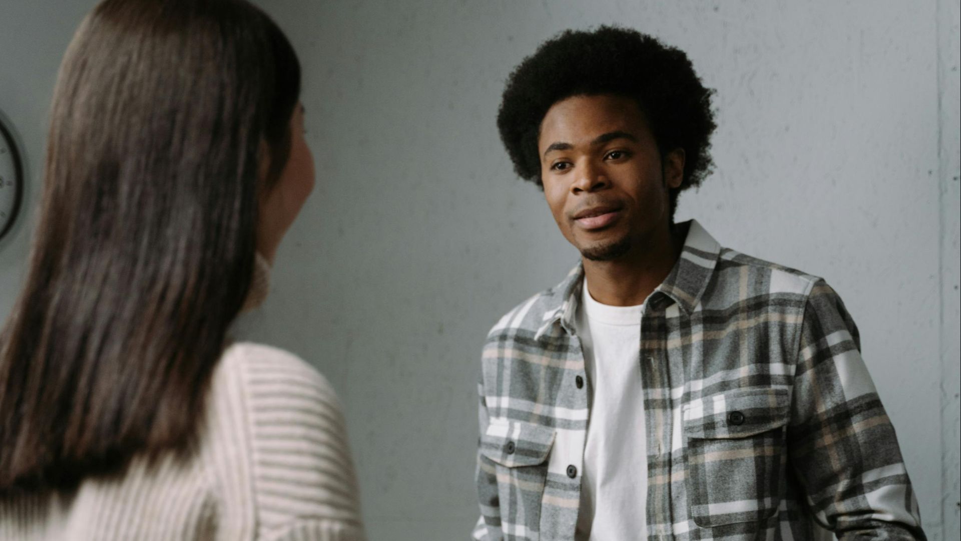 Two people in a stylish, modern room engaged in conversation, showcasing contemporary fashion.