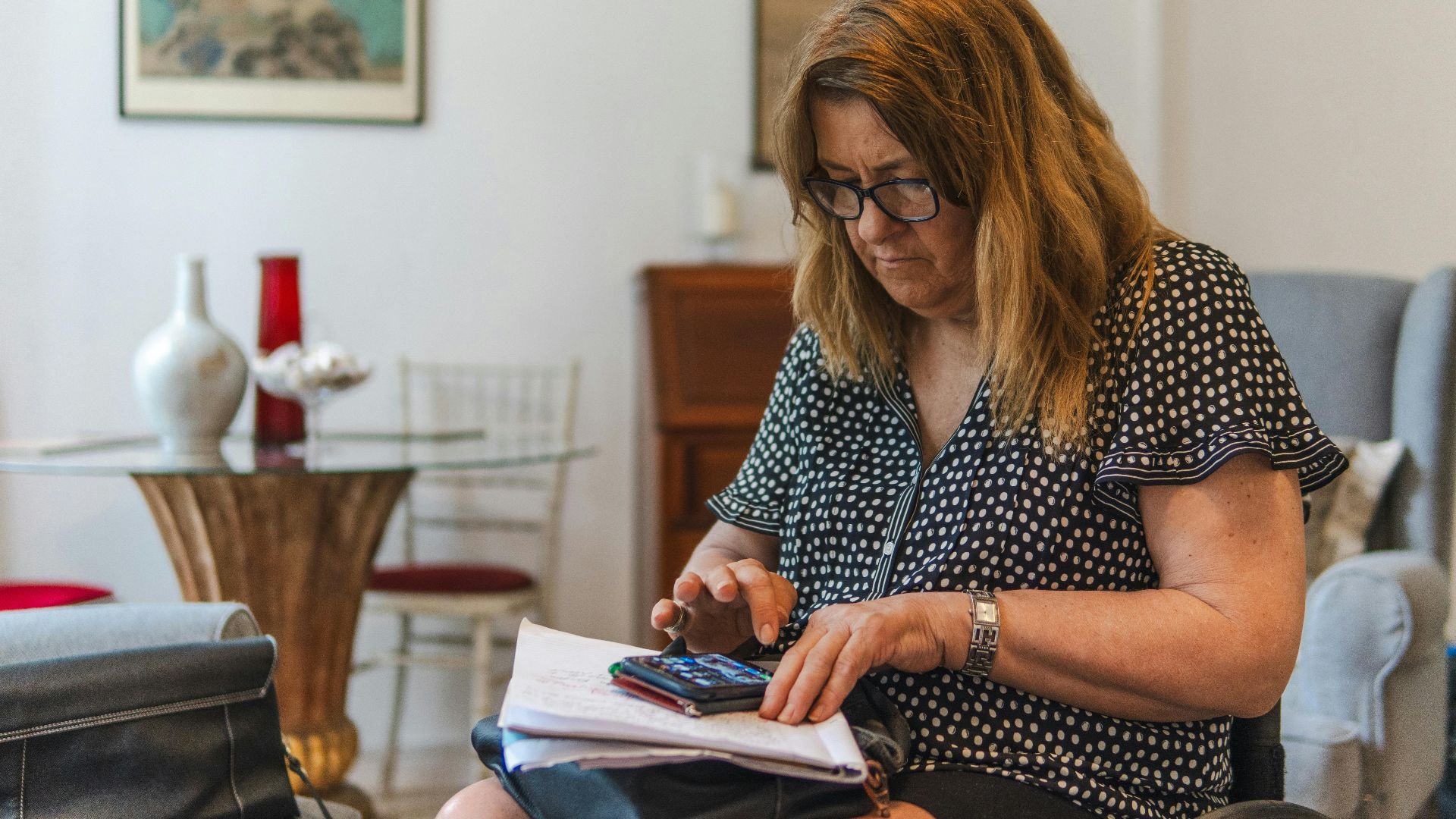 Focused woman calculating expenses with calculator and notebook at home.
