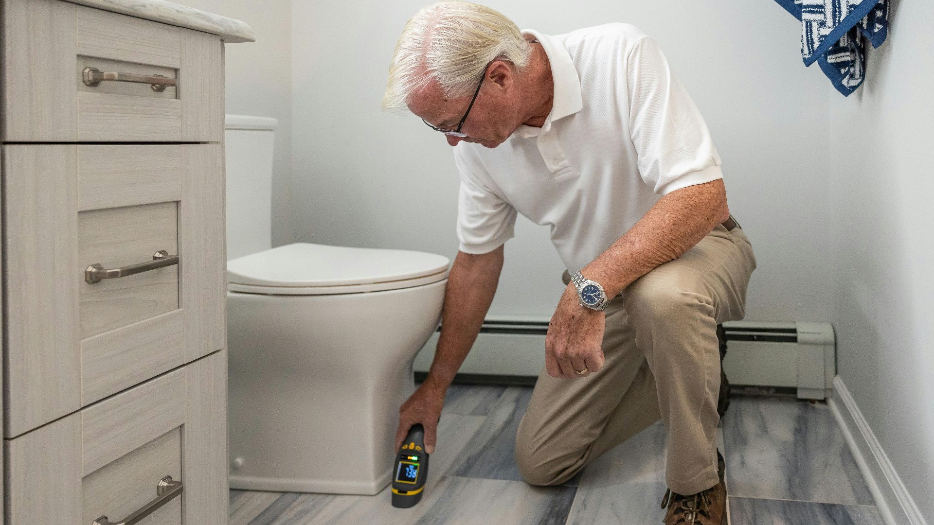A senior man using a device to inspect a bathroom for maintenance or repair.