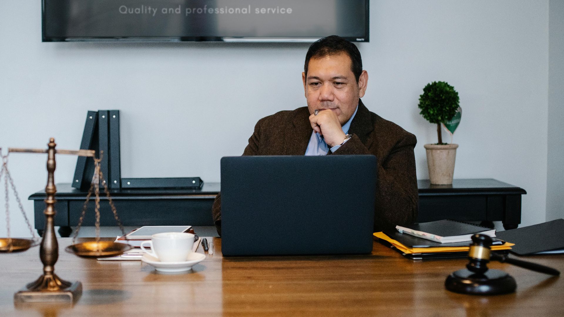 Serious ethnic mature man in formal outfit working with netbook at table with gavel
