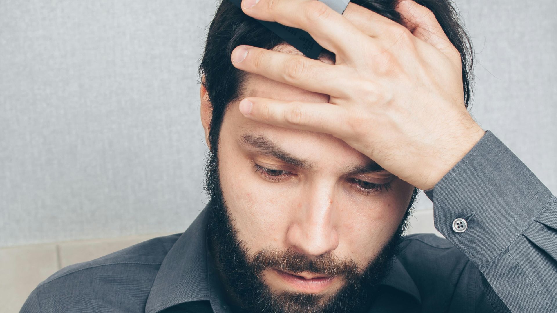 A stressed man looks at his smartphone, holding a credit card in his hand.