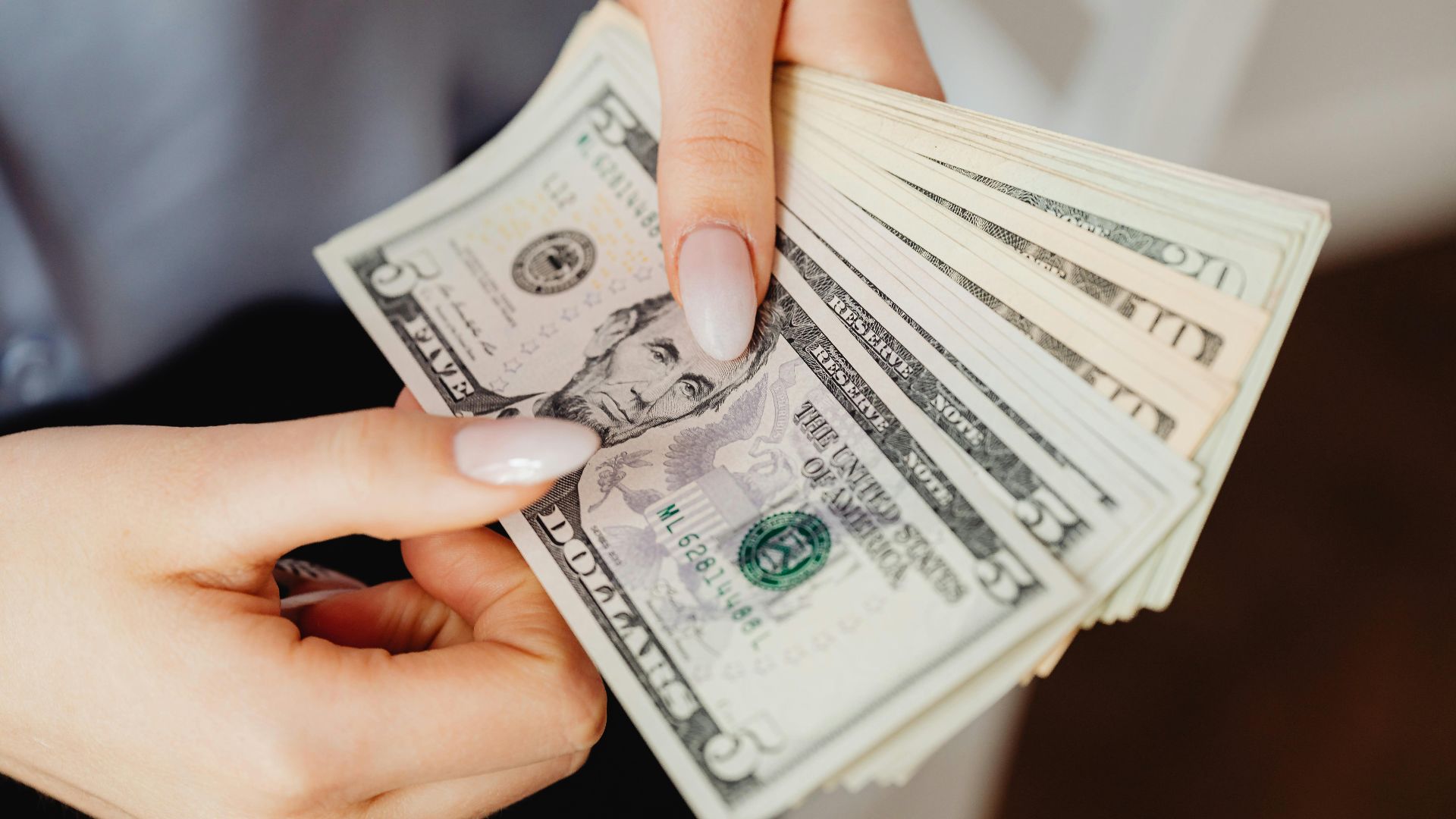 Hands count US dollar bills, showcasing finance and cash handling concepts.