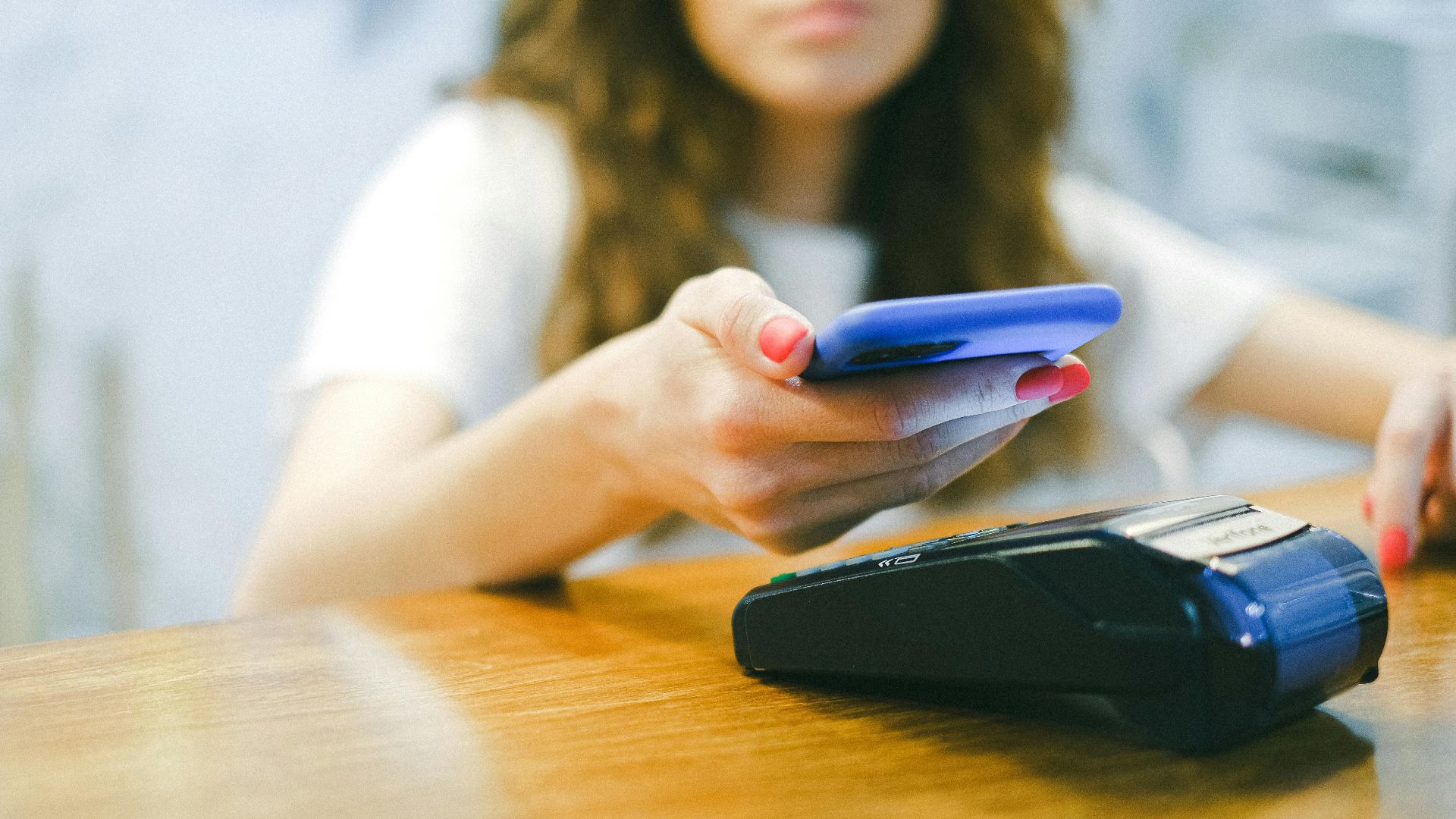 A woman processes a contactless payment using her smartphone at a payment terminal.