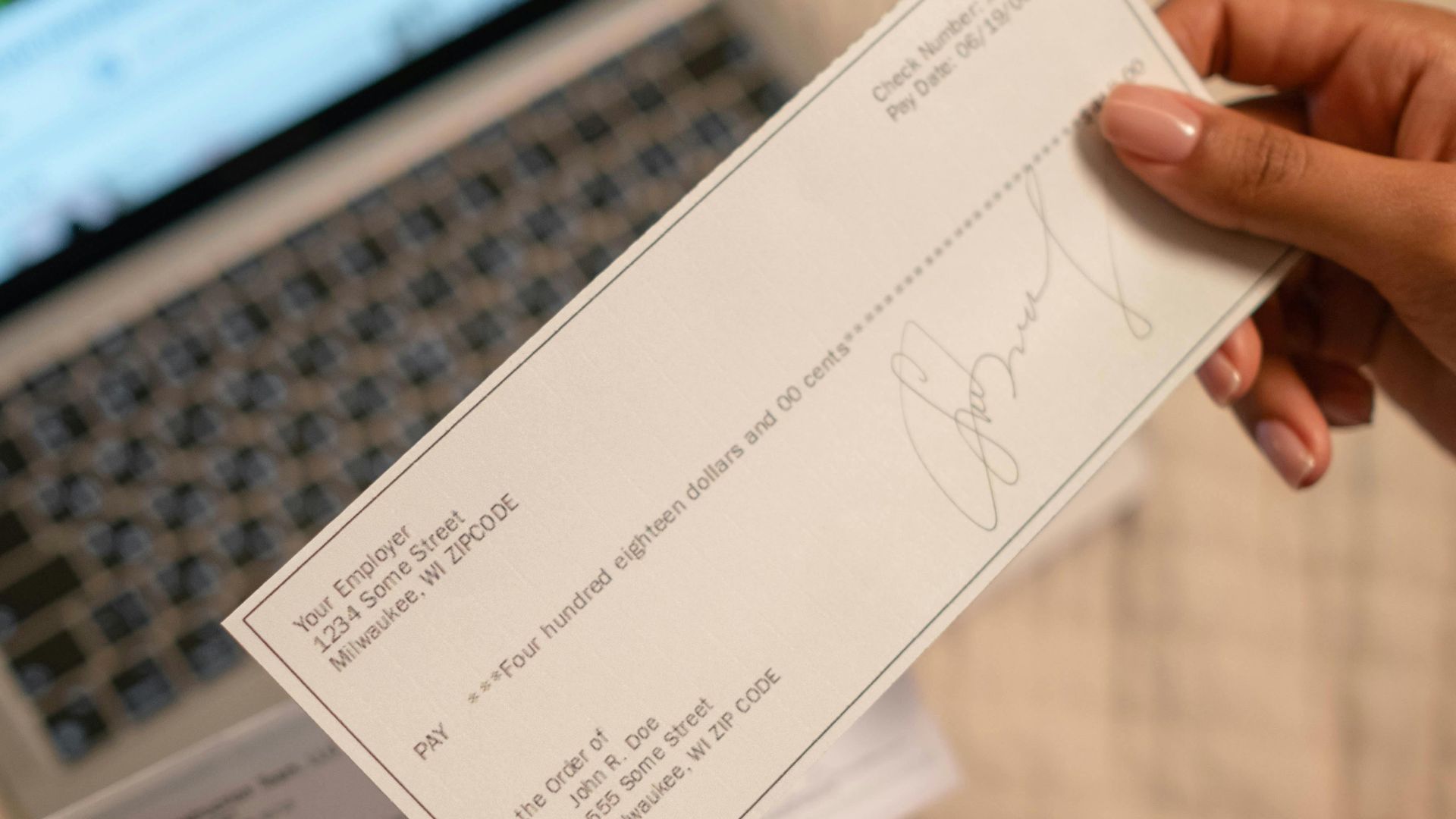 Individual holding a cheque over laptop, signifying online banking or financial transaction.