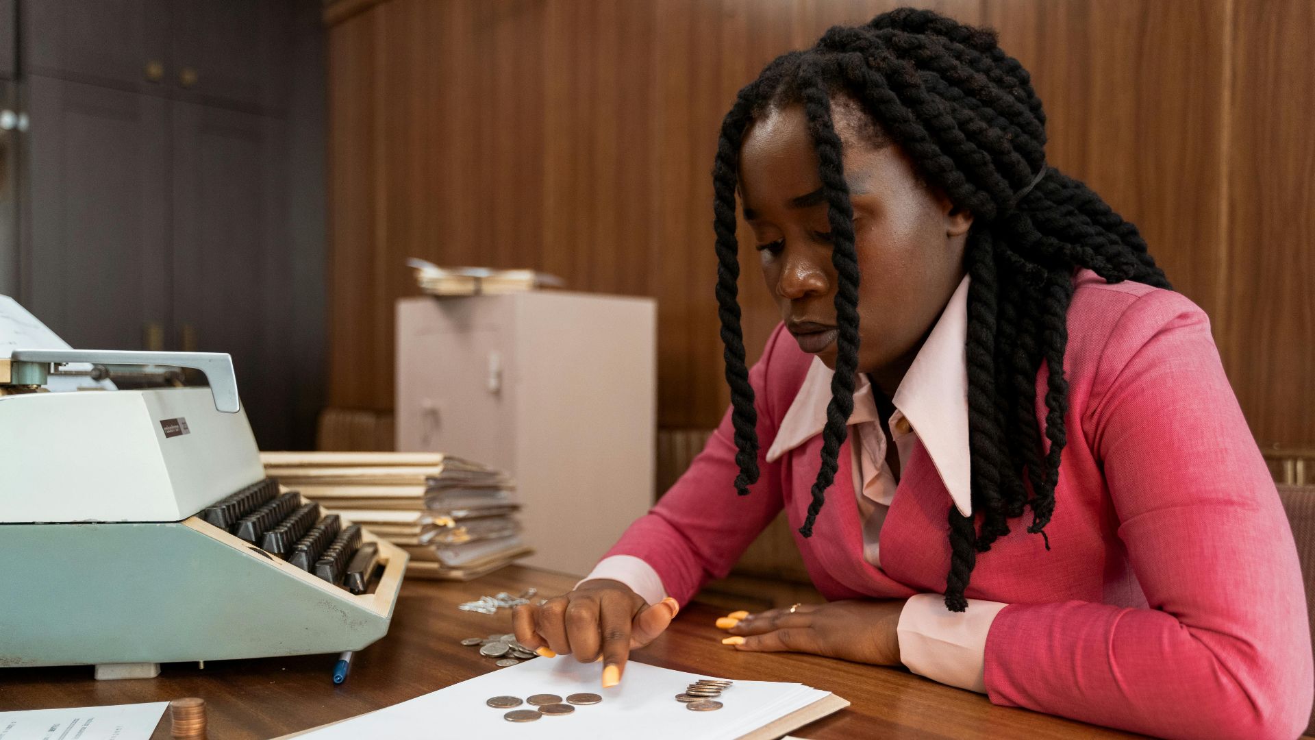 A businesswoman in vintage attire counts coins in a retro office setting.
