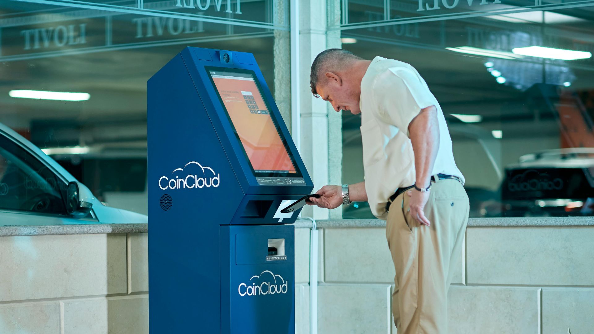 Man interacting with a blue Coin Cloud machine indoors, illustrating modern finance technology.