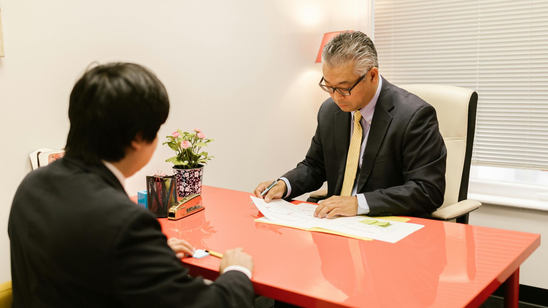 Two professionals discussing documents in a modern office with a red desk.