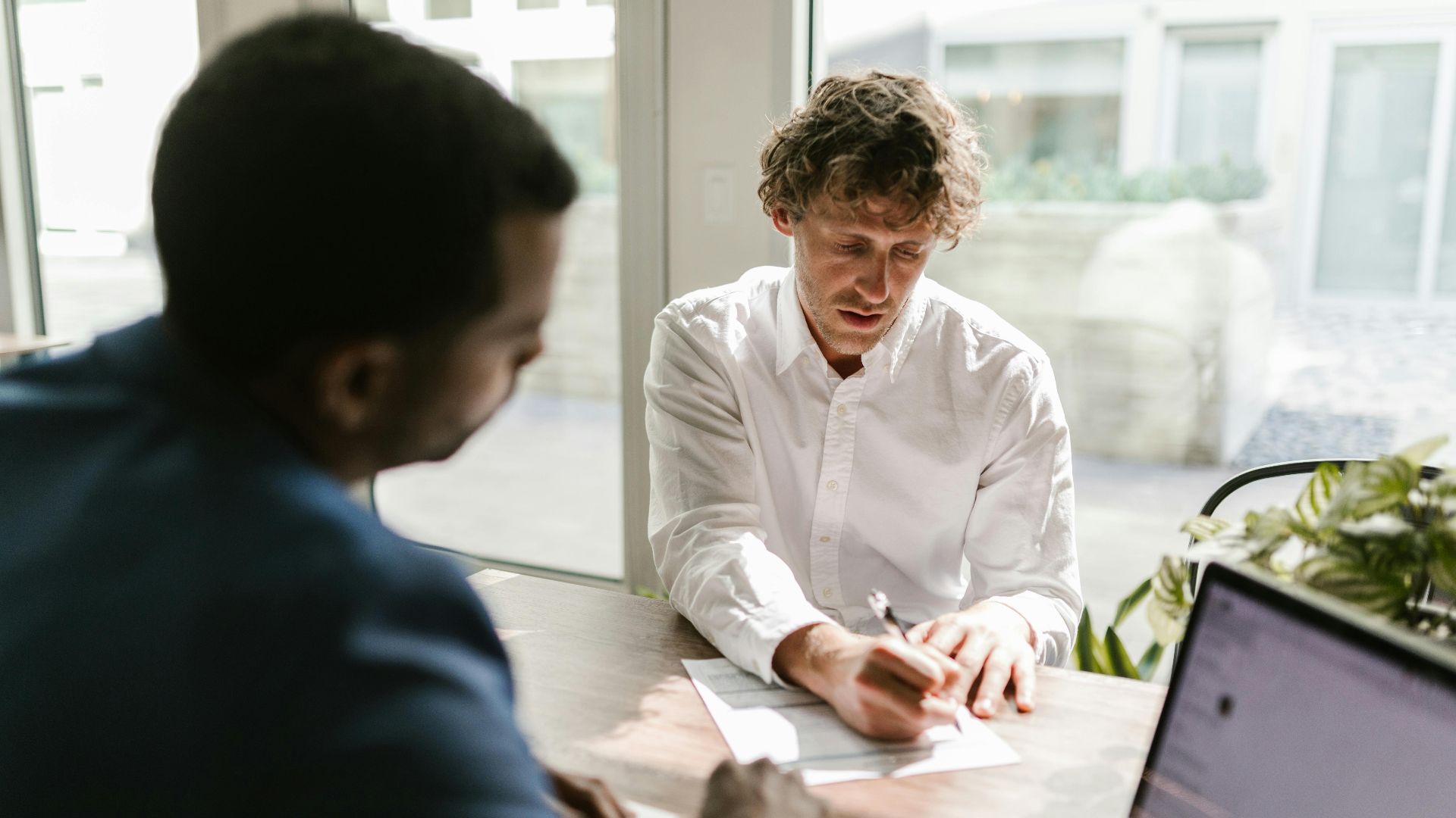 Two men collaborating in a modern office, reviewing and signing documents.