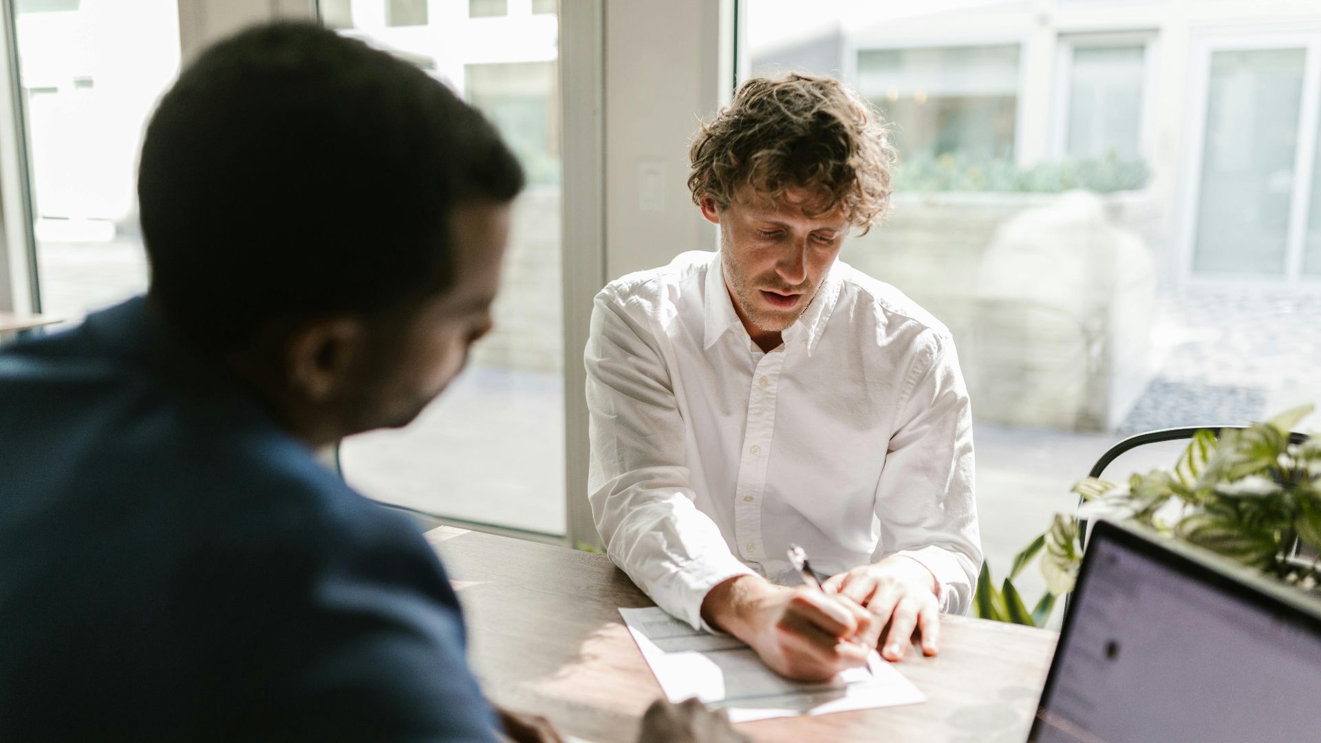 Two men collaborating in a modern office, reviewing and signing documents.