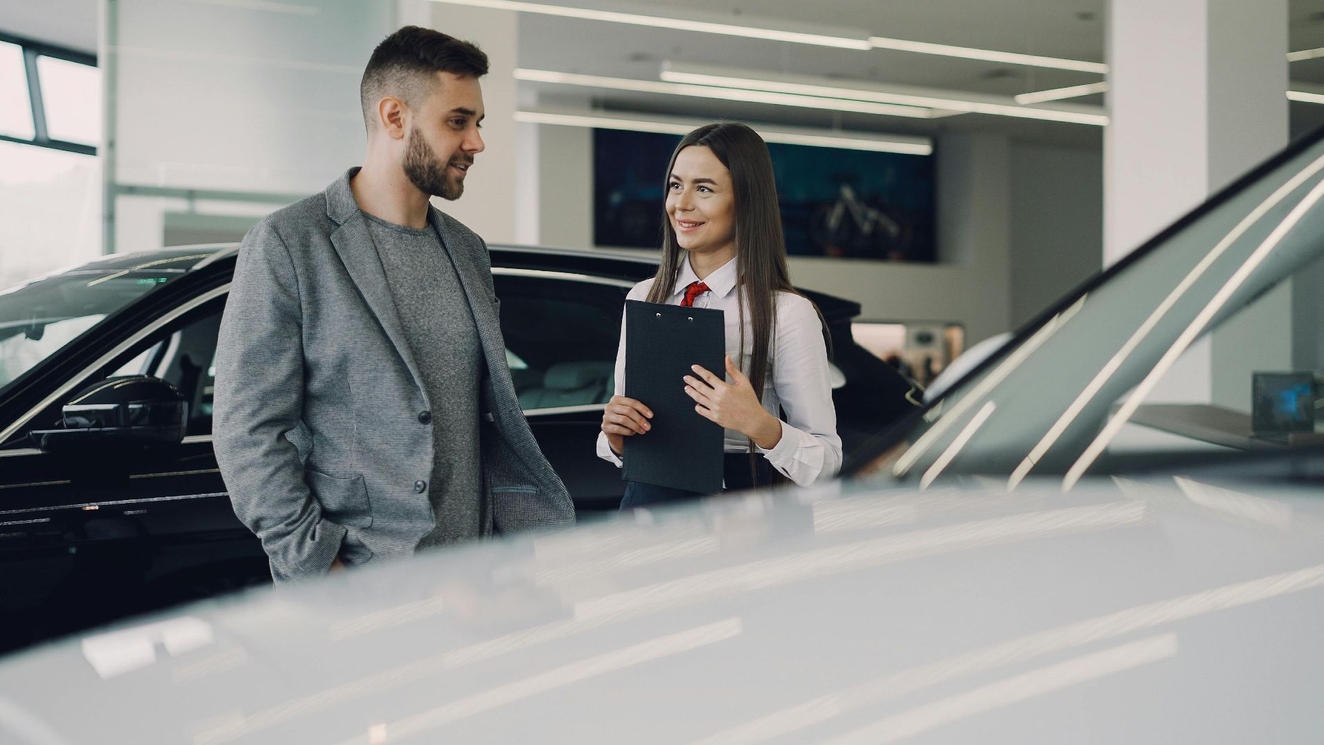 Man consults with salesperson in modern car dealership showroom.