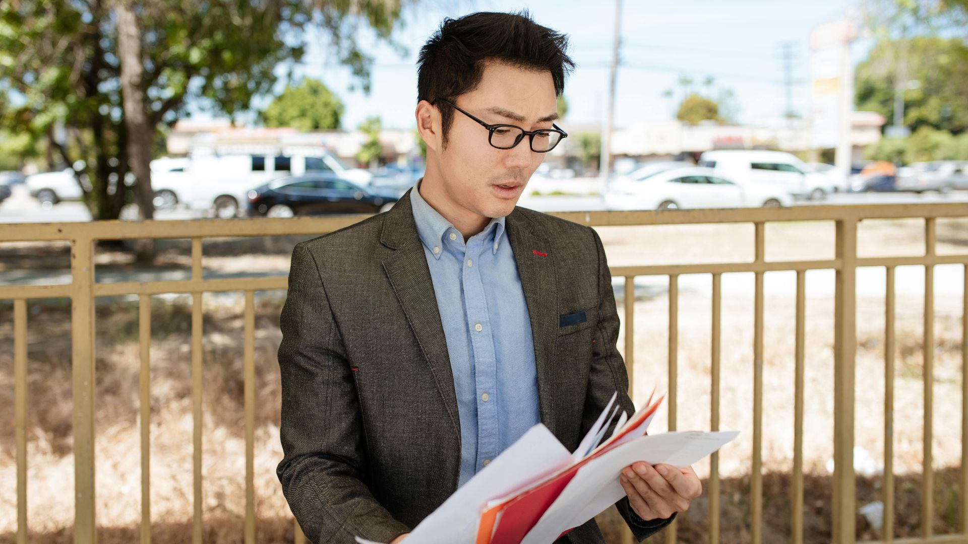 Asian businessman in a suit checking documents outdoors on a sunny day.