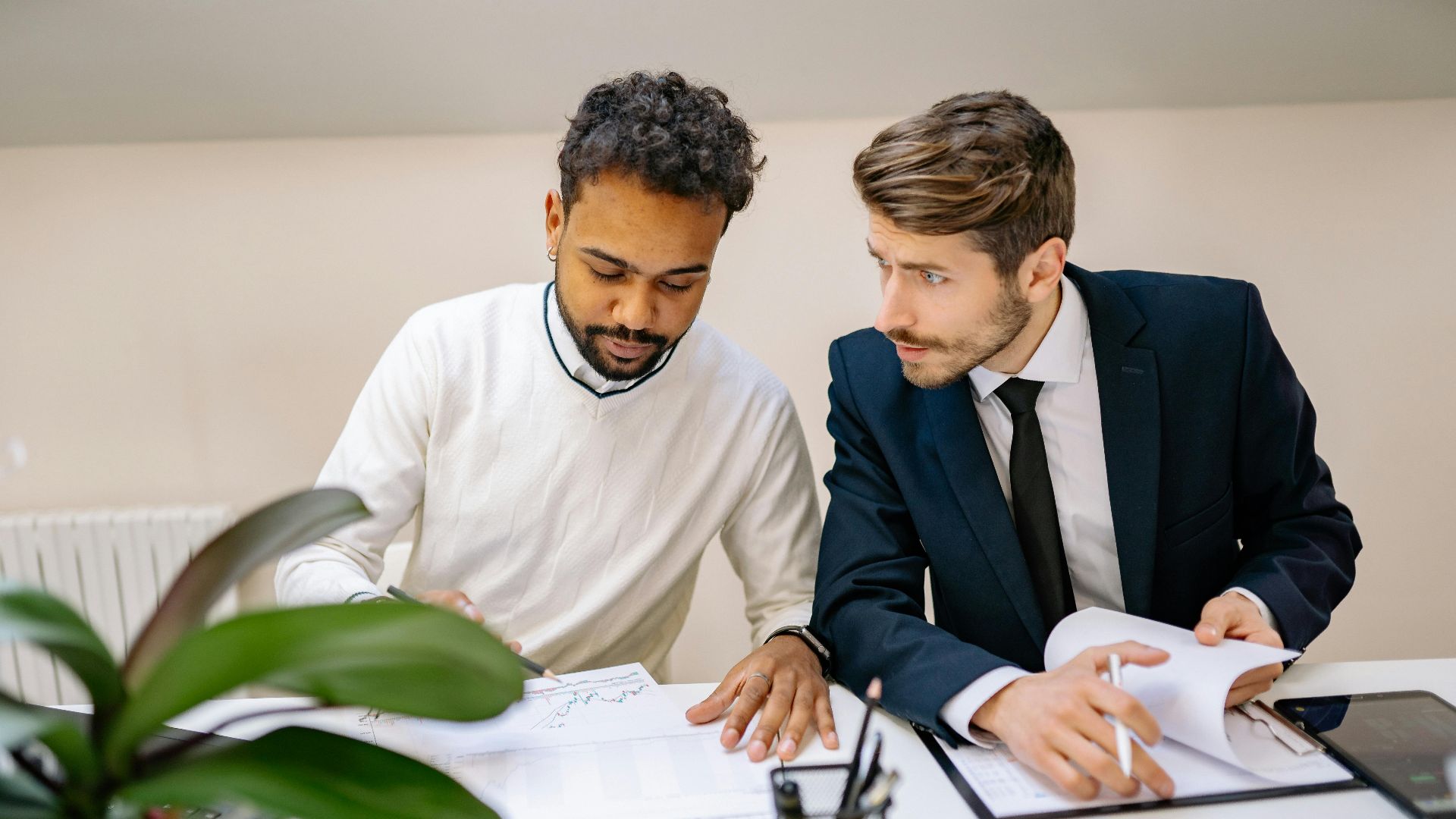 Two men in a modern office discussing and analyzing documents with charts.