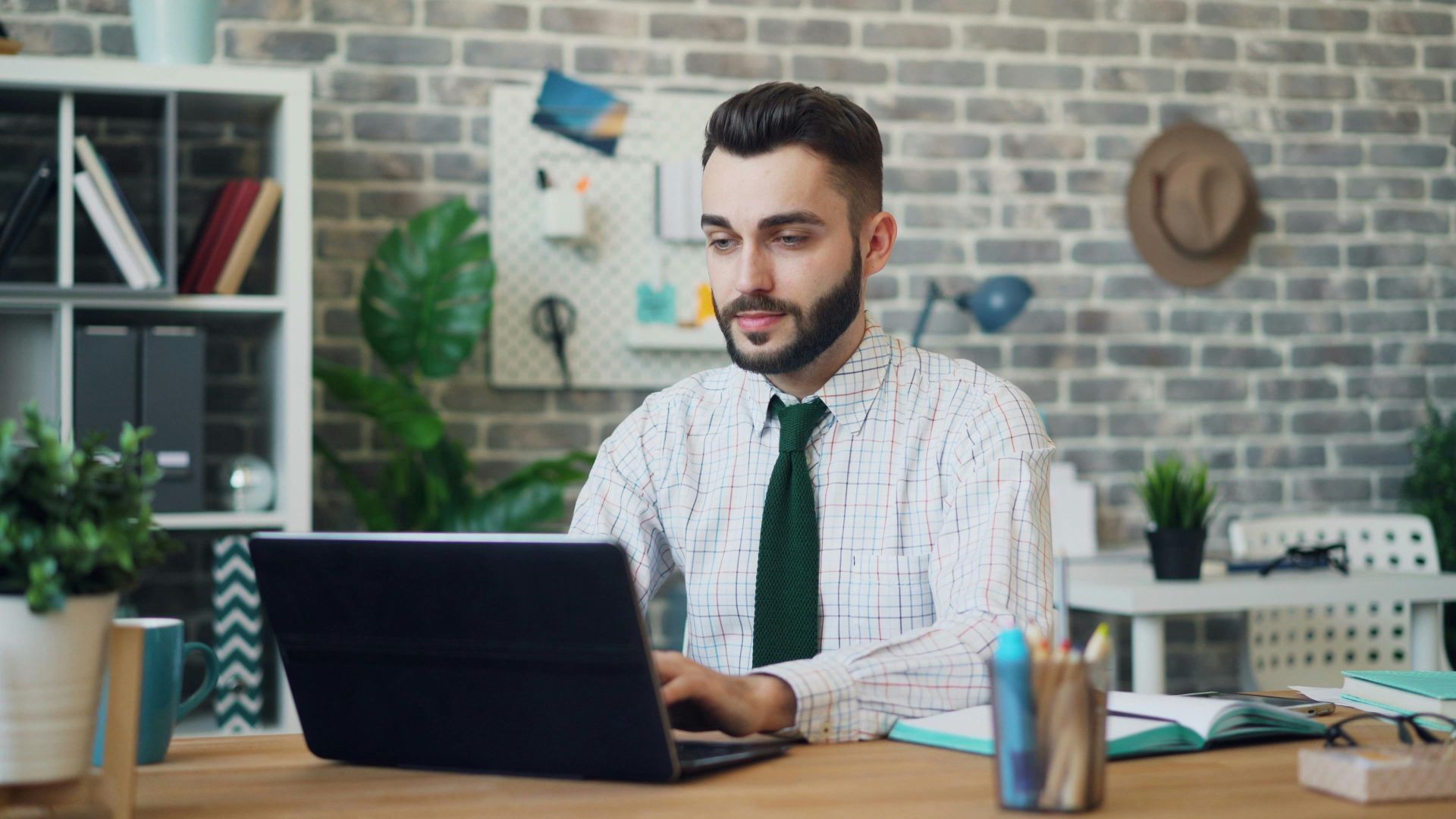 A young man in a modern office setting working on a laptop, showcasing a stylish and contemporary workspace.