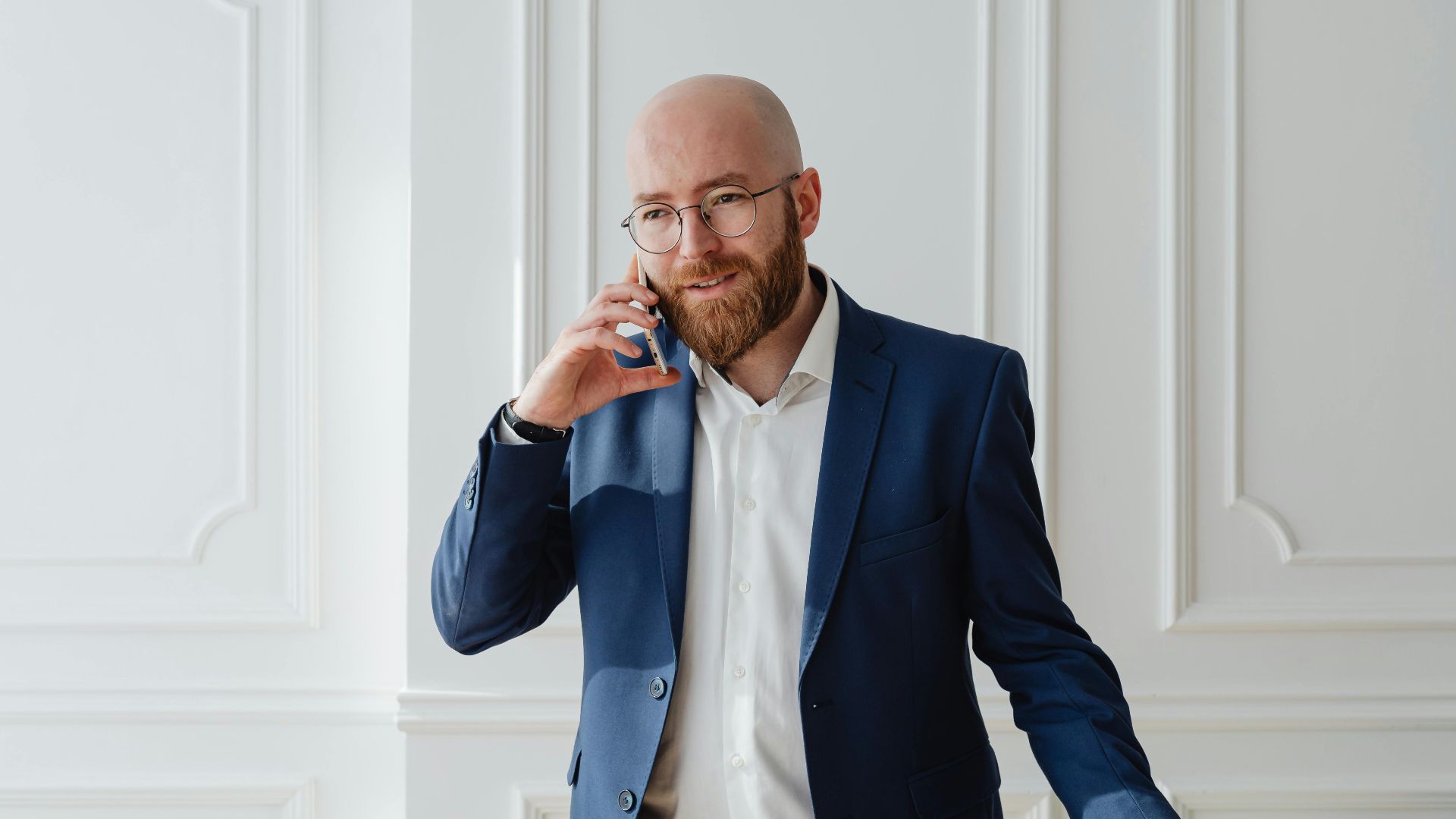 Bald bearded businessman in a suit having a phone call indoors.