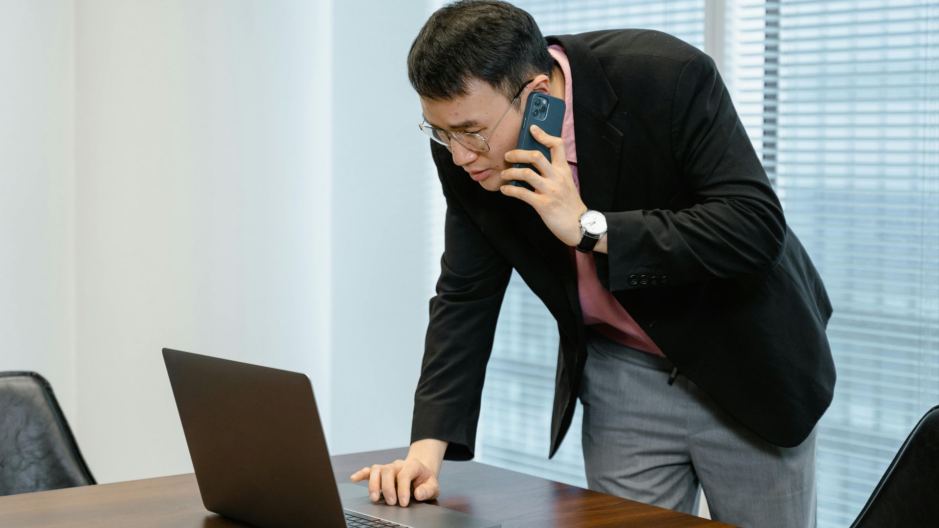 Asian businessman in the office multitasking with a laptop and smartphone call.