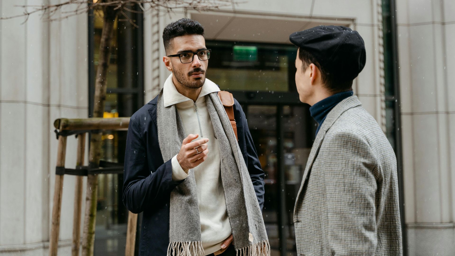 Two businessmen engaged in conversation outside in winter attire with snow falling lightly.