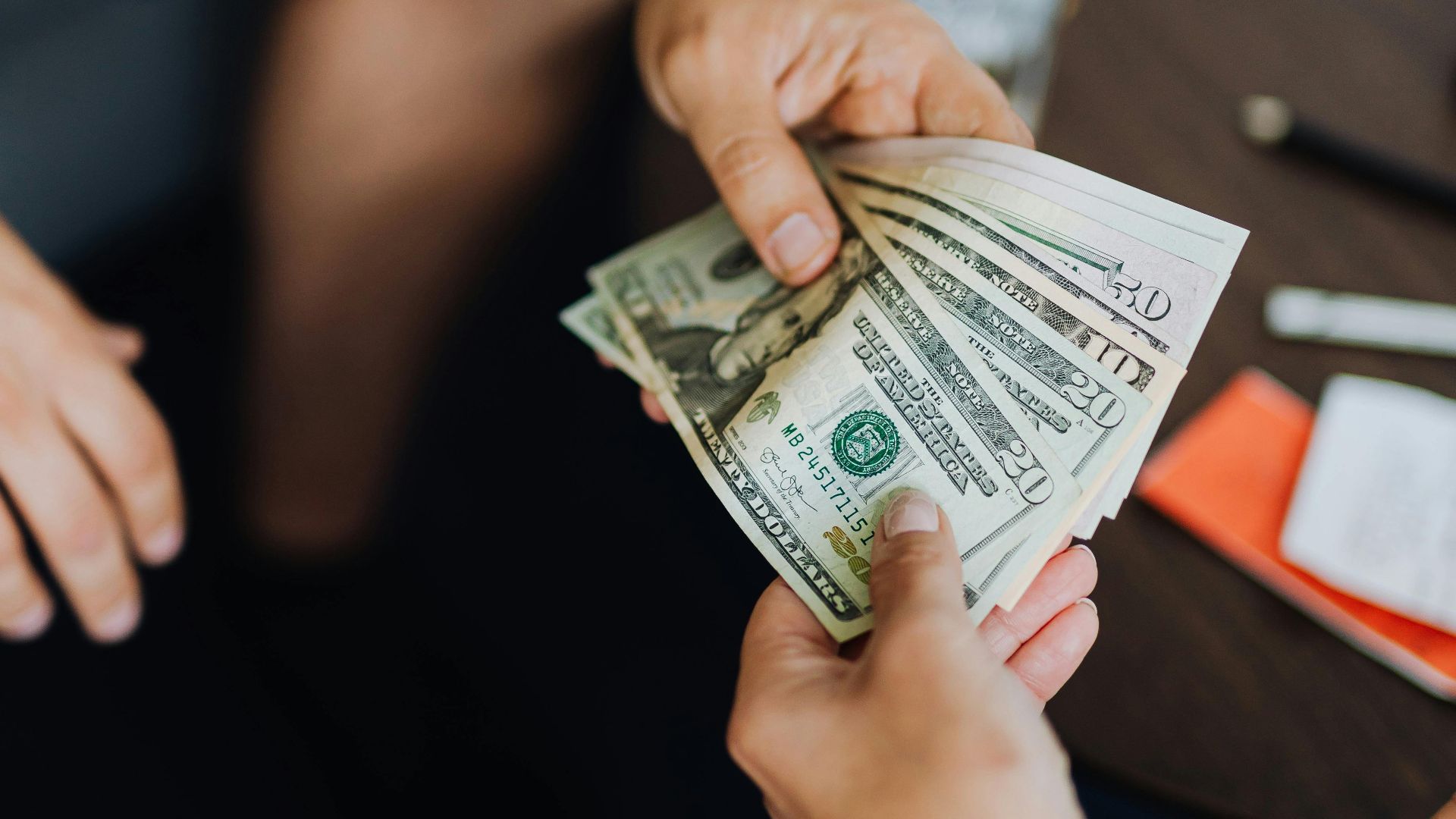 A close-up view of hands exchanging dollar bills indoors, symbolizing payment.