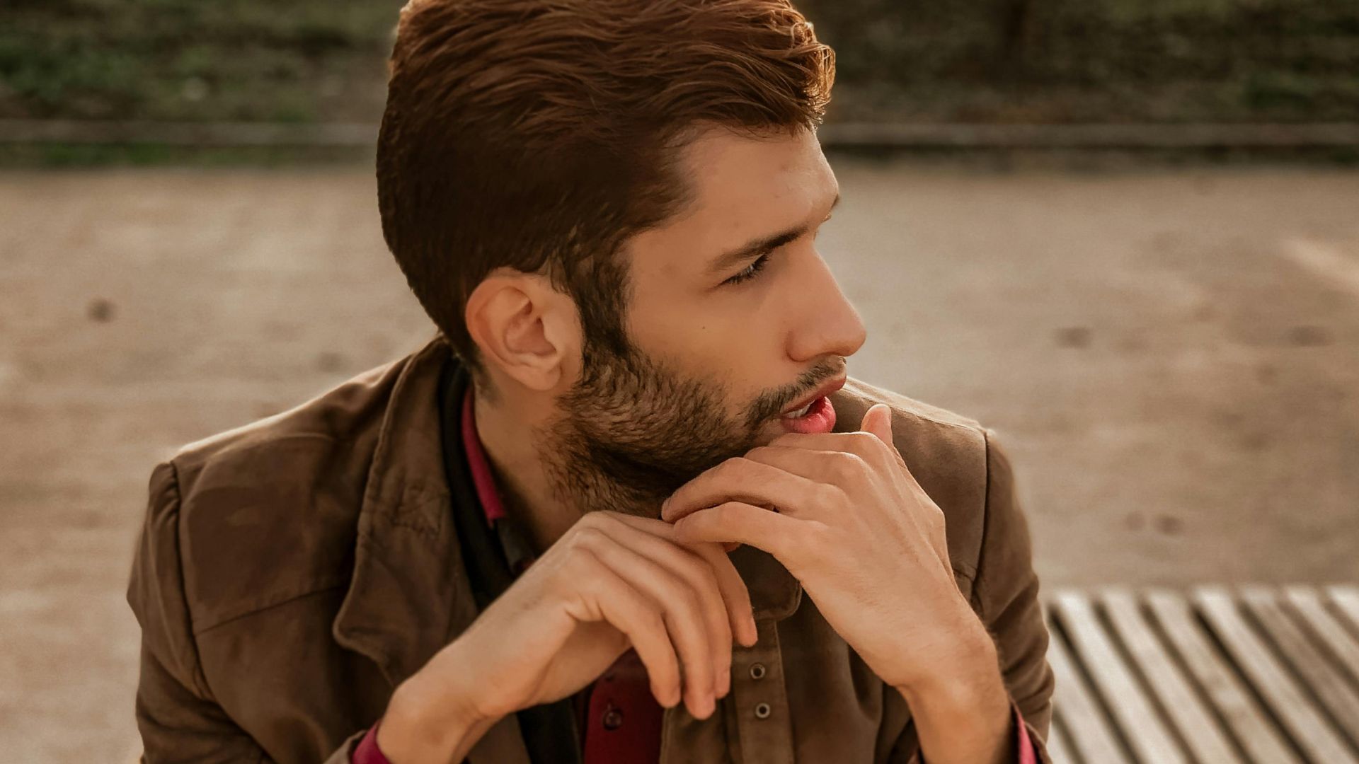 Casually dressed man sits outdoors on a bench, lost in thought. Warm evening light.