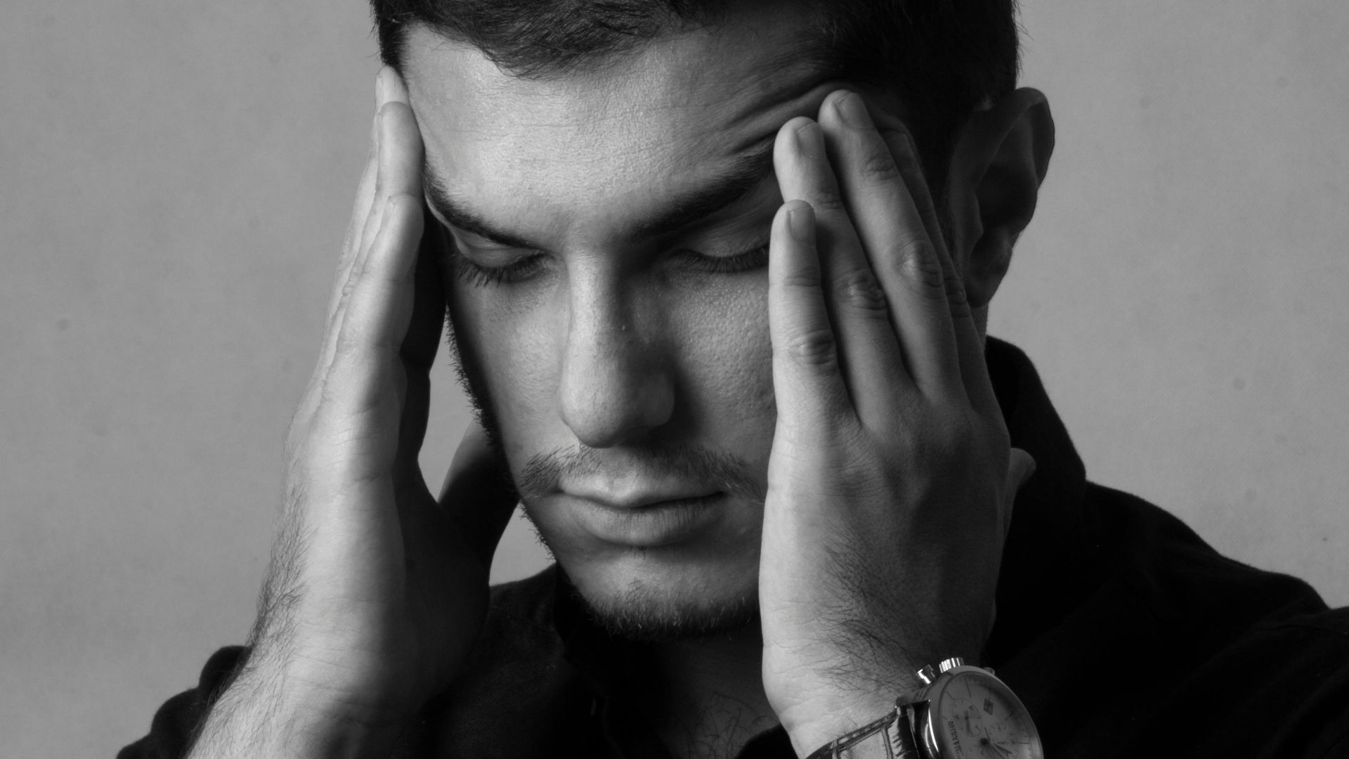 Close-up black and white portrait of a man holding head, indicating stress or headache.