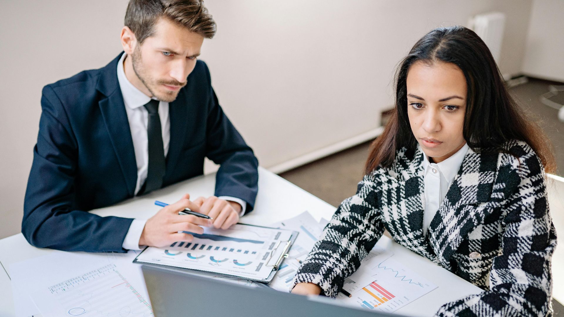 A man and woman collaborate on business analysis at a desk with charts in an office setting.