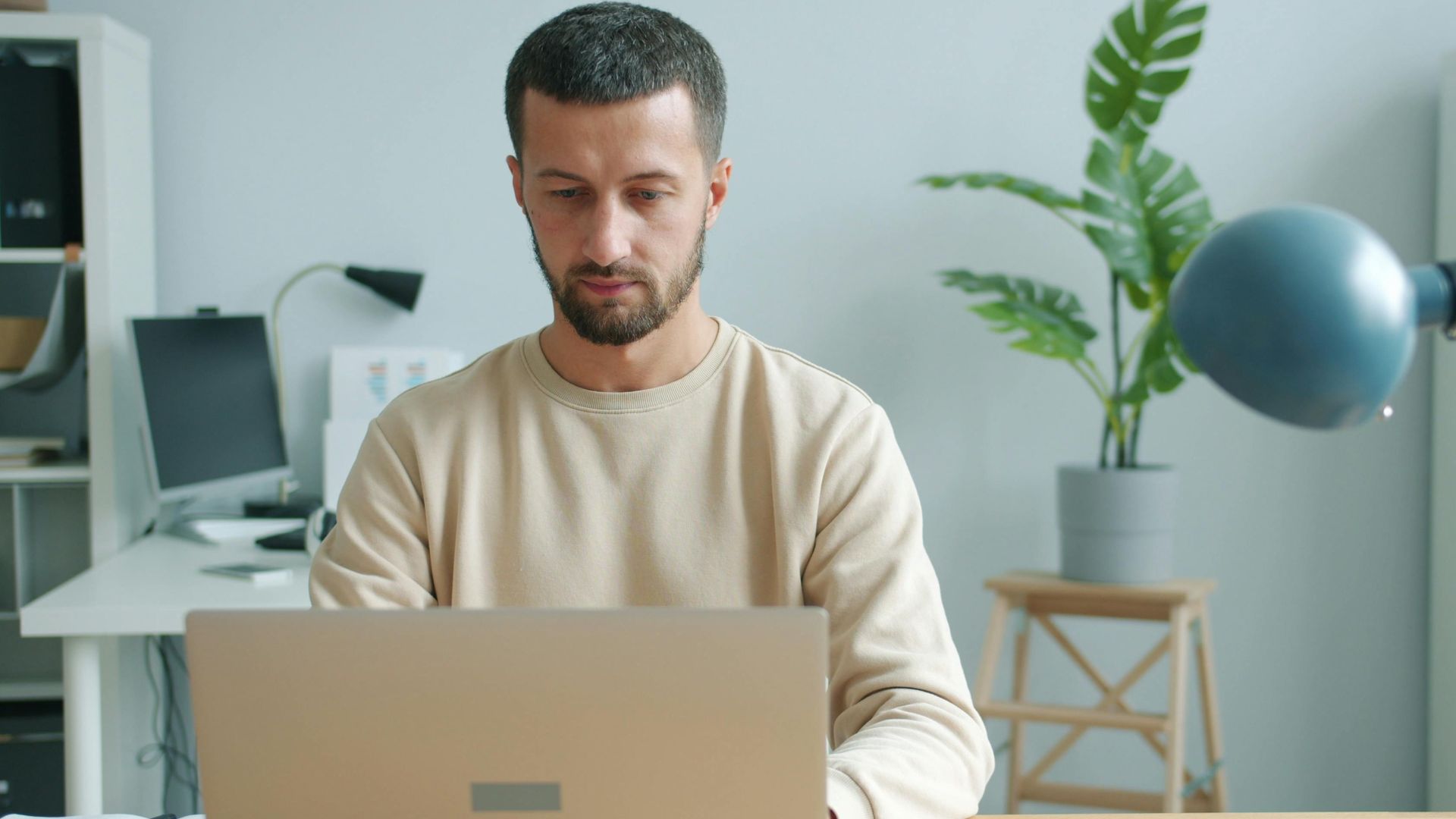 A man in a bright office environment focused on his laptop work.