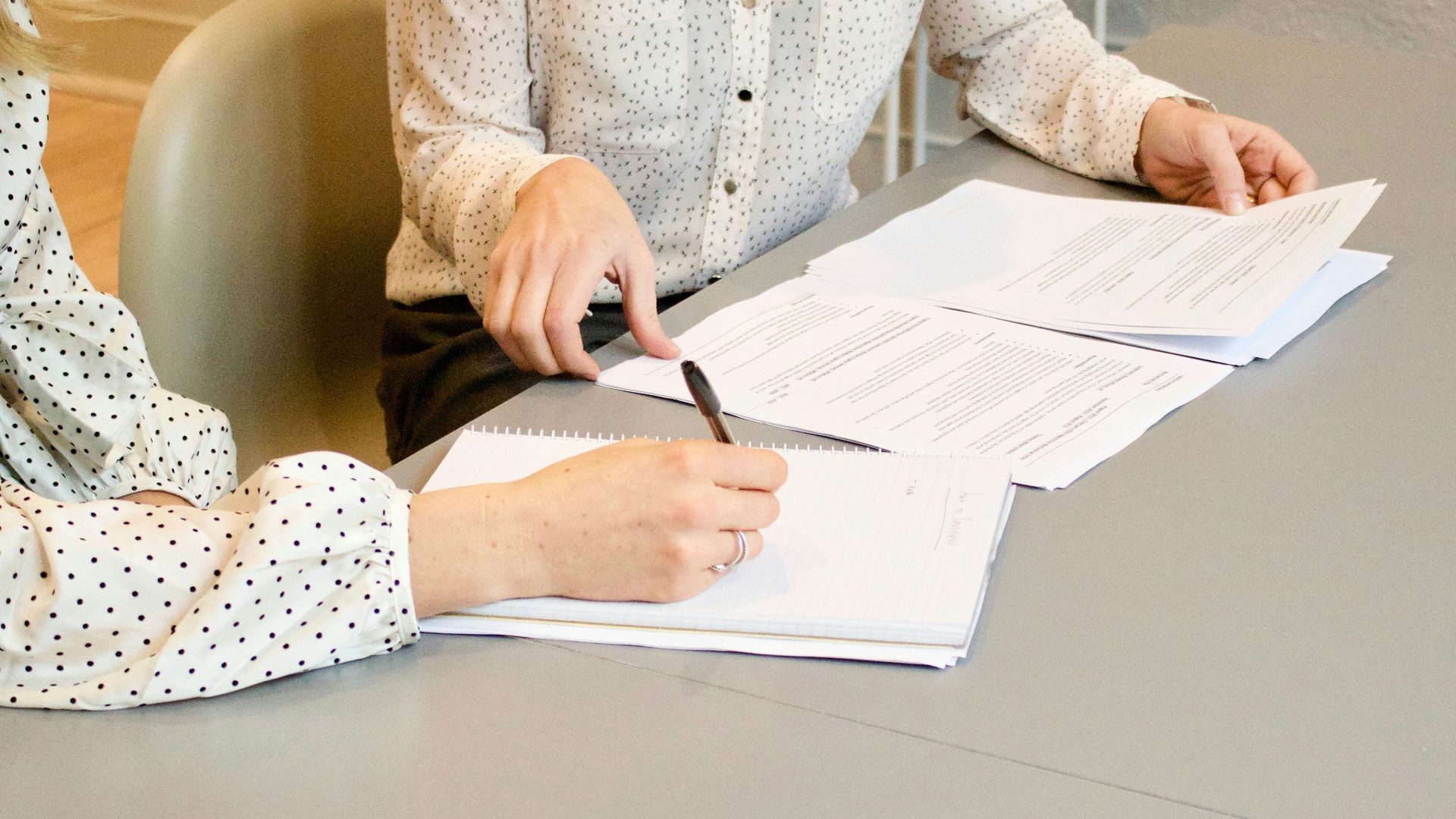 woman signing on white printer paper beside woman about to touch the documents