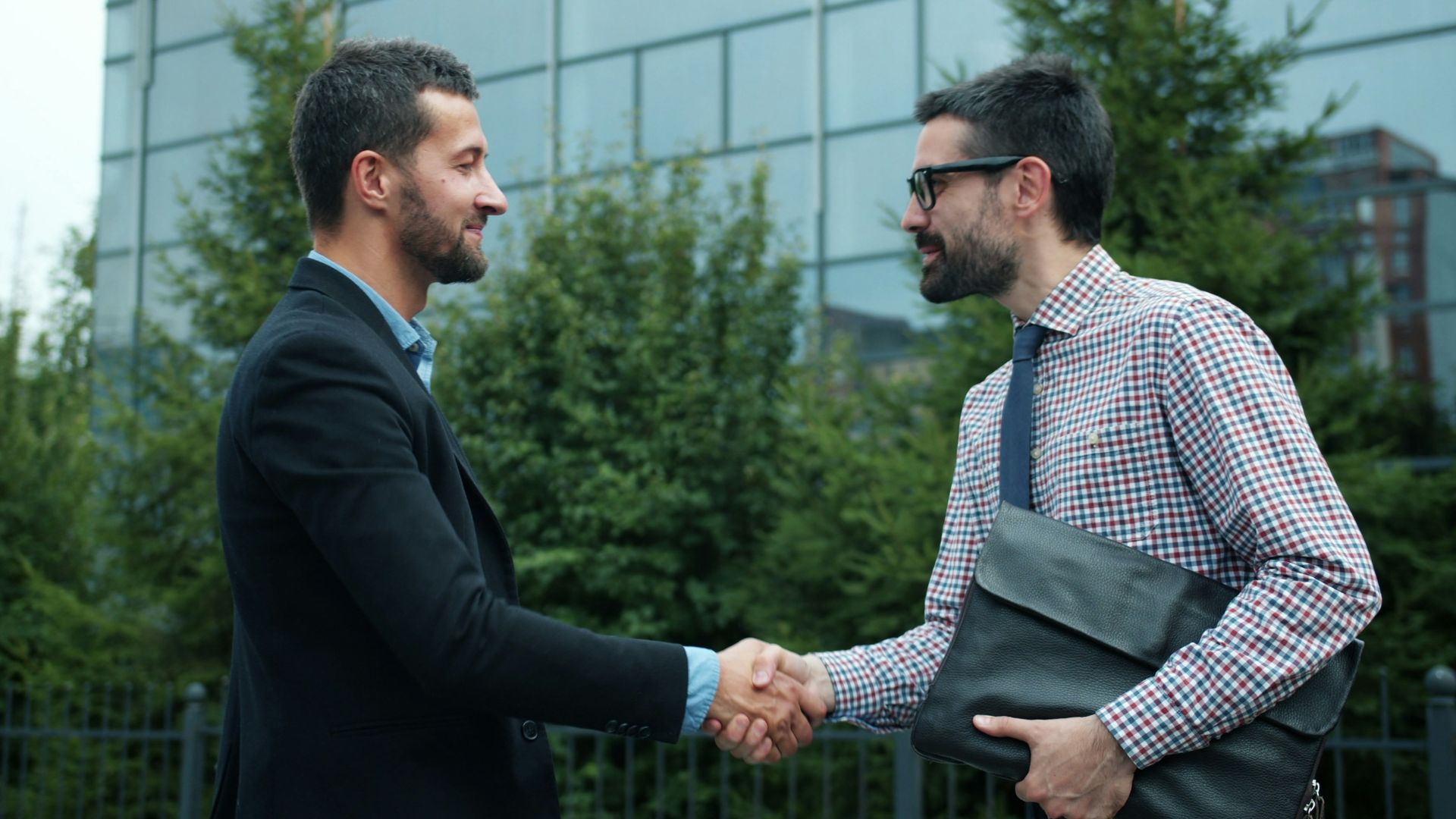 Two businessmen shaking hands outside modern building
