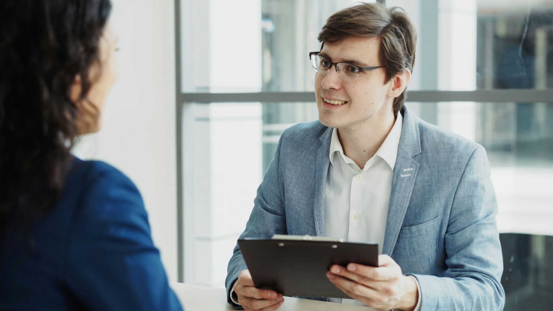 Man in suit interviews woman holding clipboard.