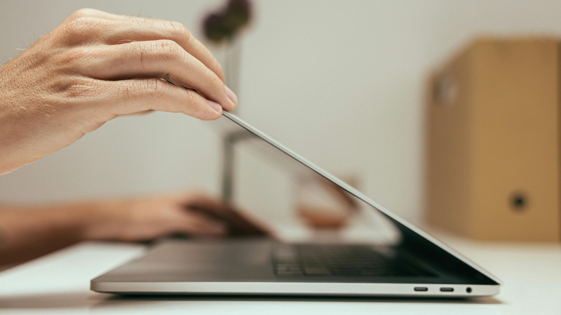 A close-up of a hand closing a laptop in a clean and minimal office setting, symbolizing the end of a work session.