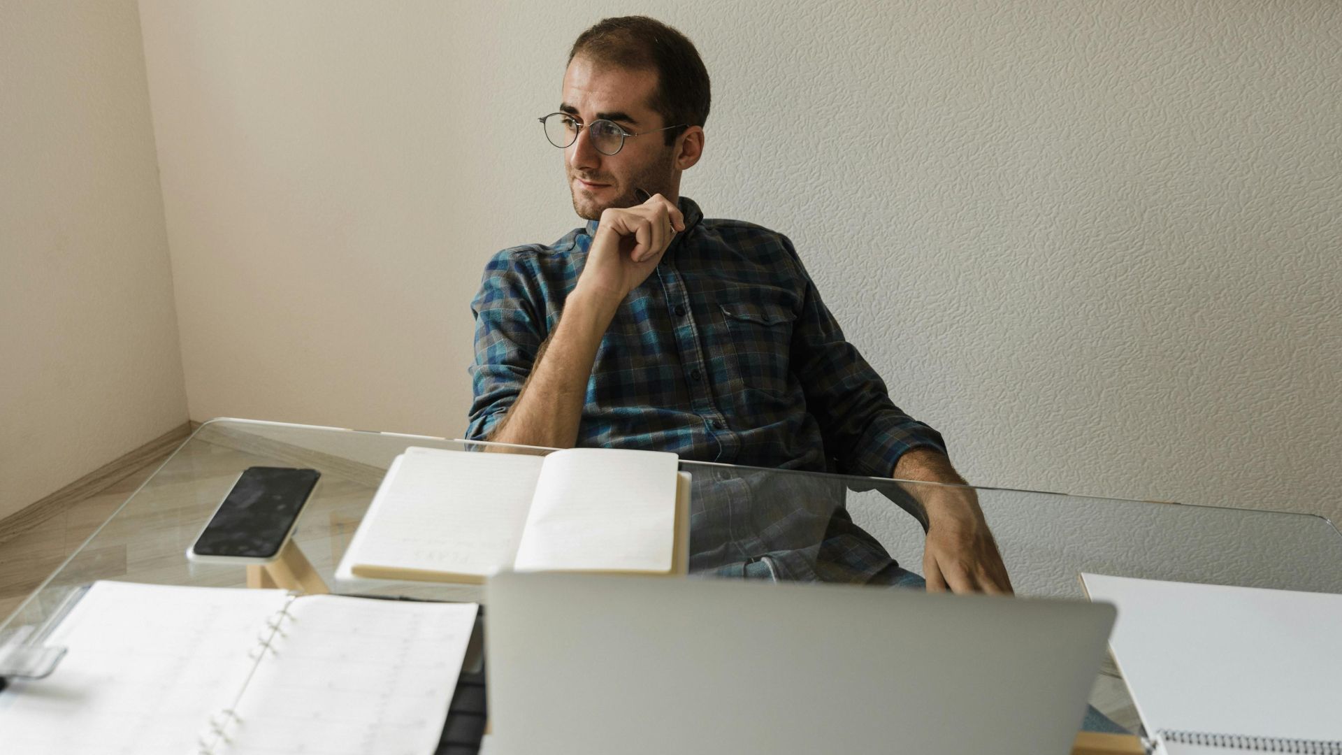 Caucasian man with eyeglasses pondering at workplace with open notebook.