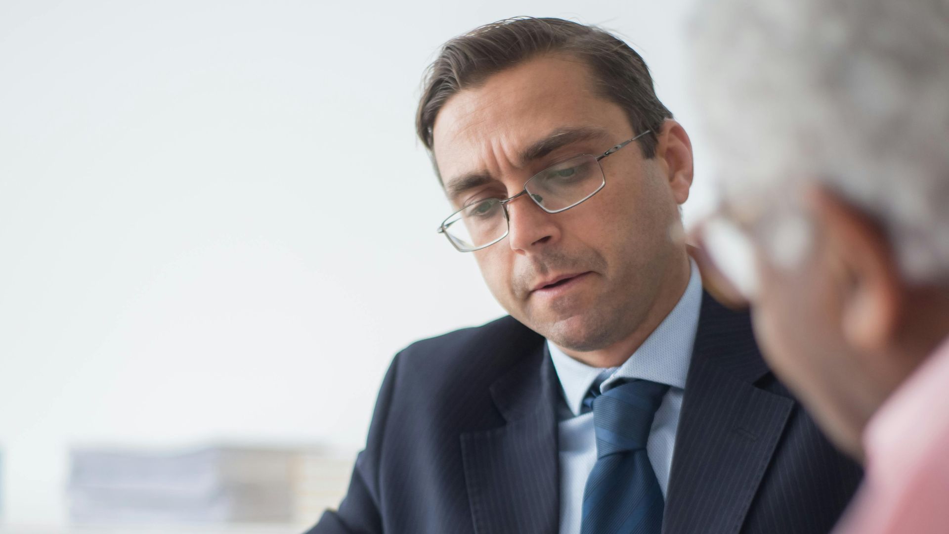 Senior man in discussion with consultant in office setting, reviewing documents.