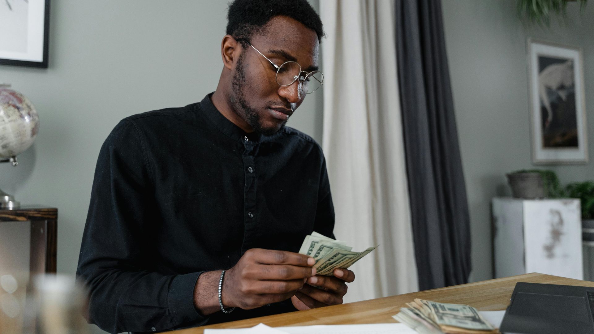 A focused man in glasses counting cash at a desk, indicating financial management.
