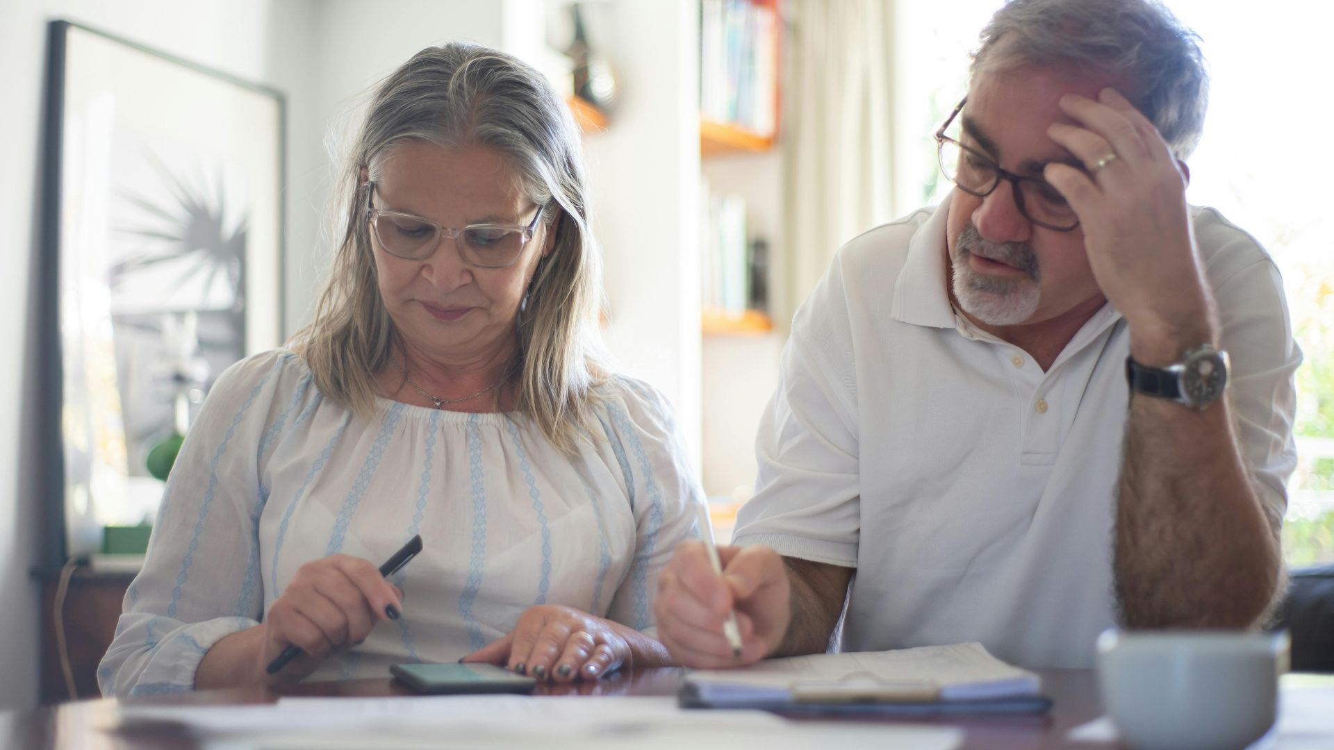 Senior couple calculating expenses at home office desk with documents and notes.