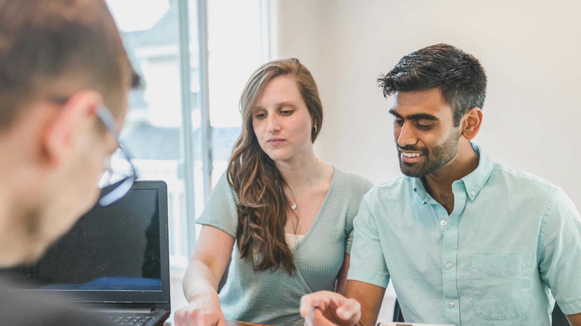 Young couple consulting with a financial advisor using a calculator and documents in a bright office setting.