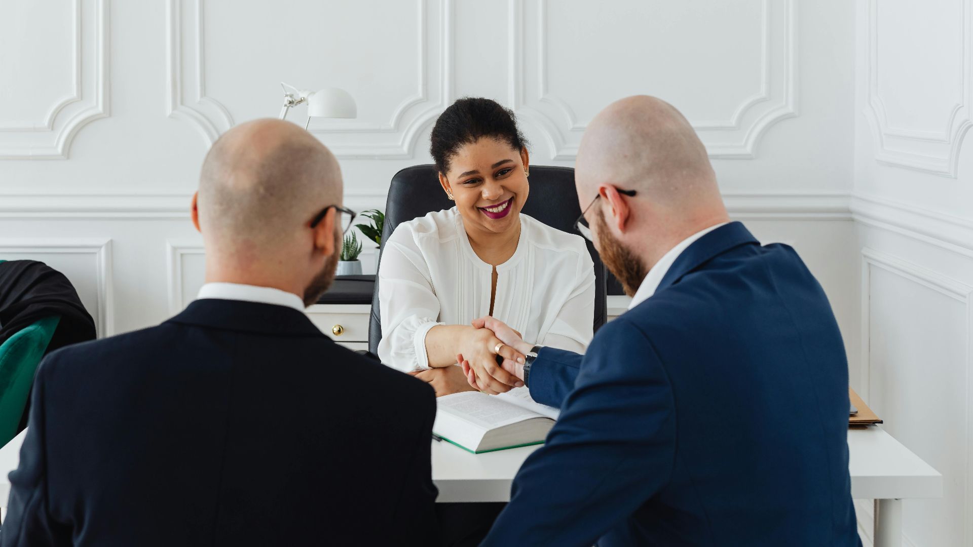 Diverse professionals in a business meeting, shaking hands across a table, indoors.