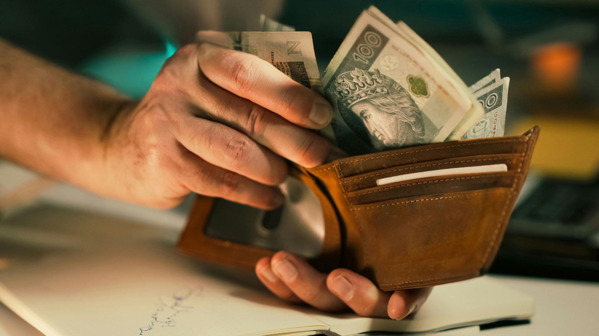 A close-up of hands holding a wallet filled with Polish banknotes on a desk.