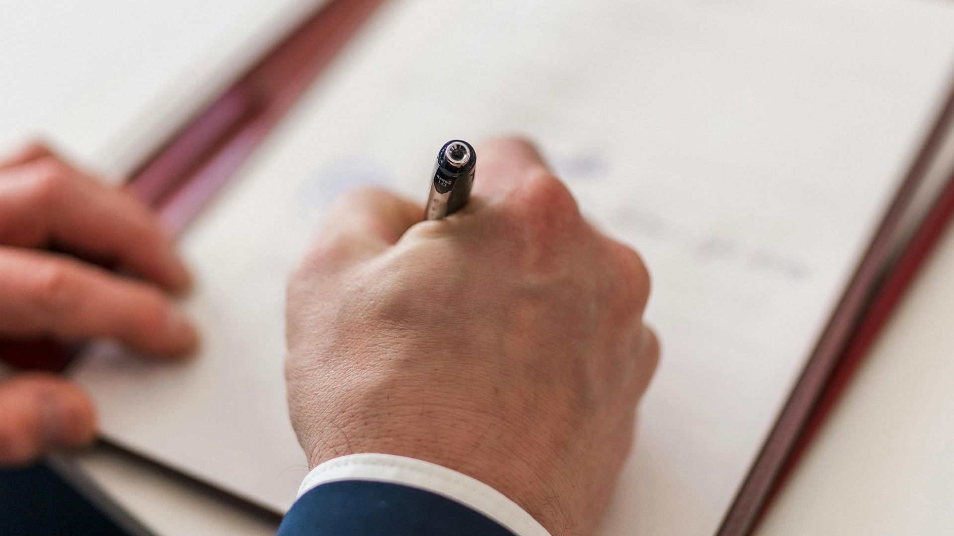 Close-up of a businessman signing a document in a formal office environment.